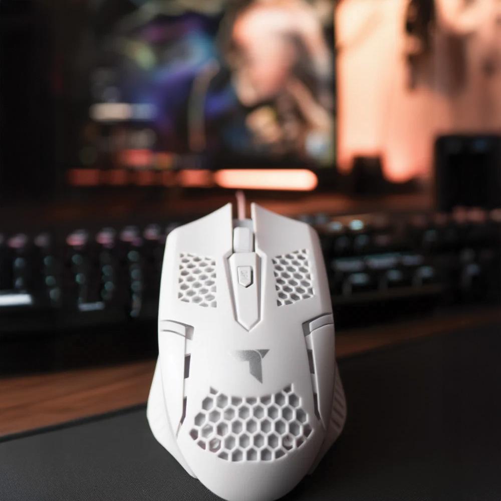 Siyah bir mousepad üzerinde beyaz bir oyun faresi. Arka planda bir klavye ve monitör var. Fare petek tasarımına sahip.