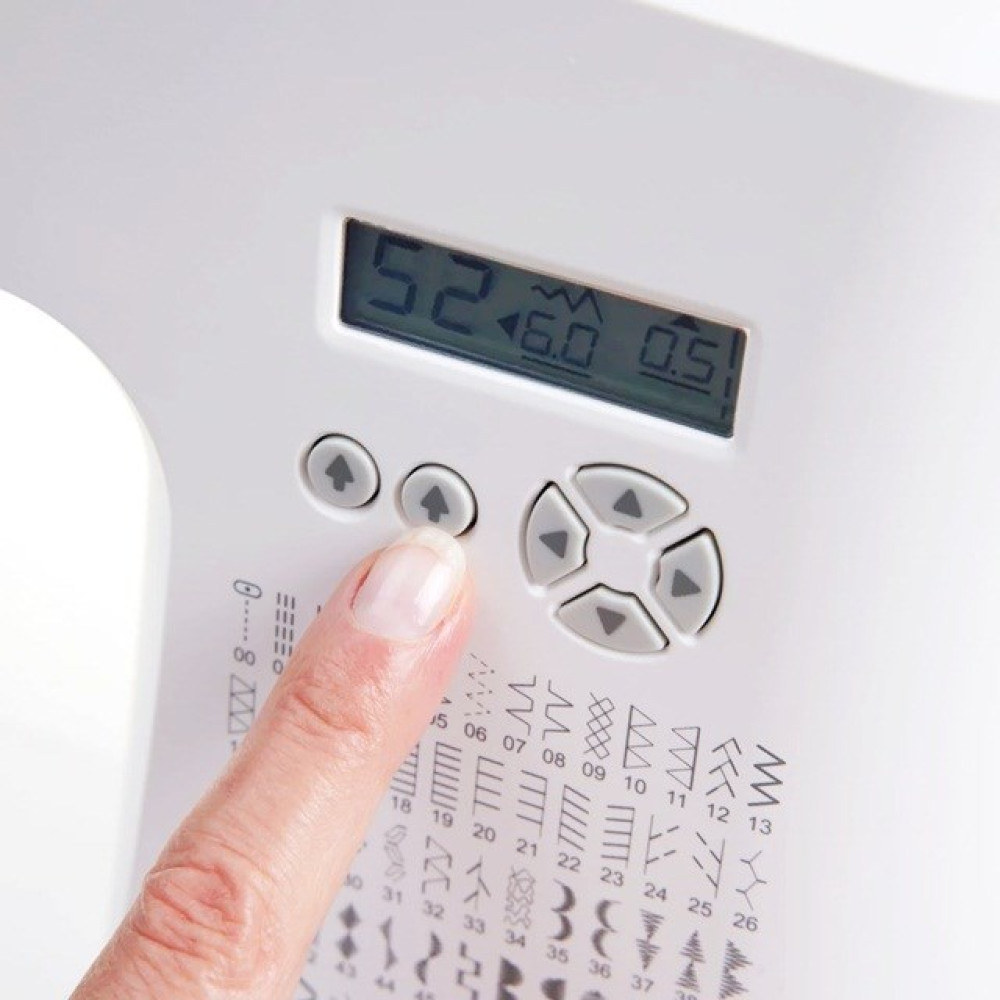 Palec naciska przycisk na maszynie do szycia. Wyświetlacz pokazuje liczby. Na powierzchni maszyny wydrukowane są opcje wzorów.