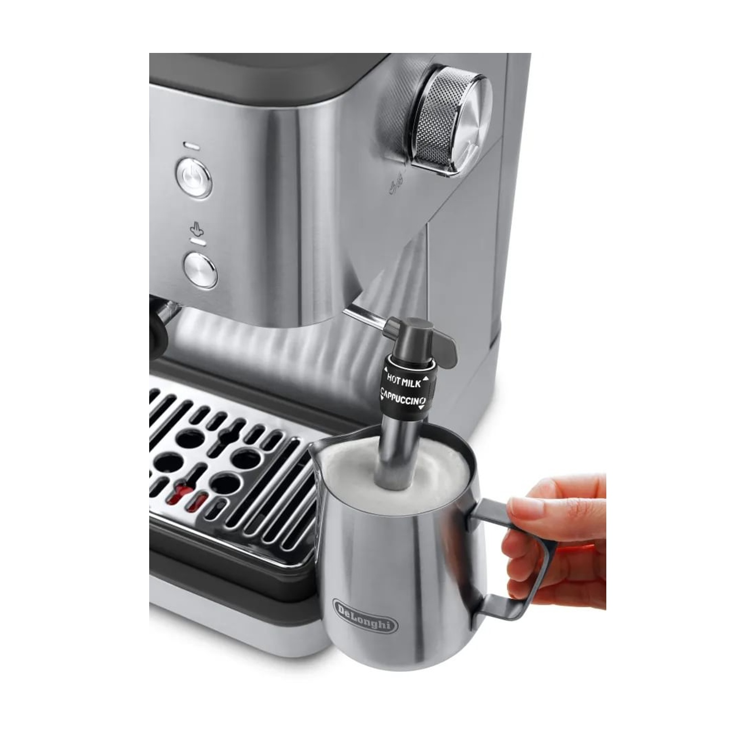 Una máquina de espresso de acero inoxidable bate leche en una jarra de metal. Una mano sostiene la jarra.