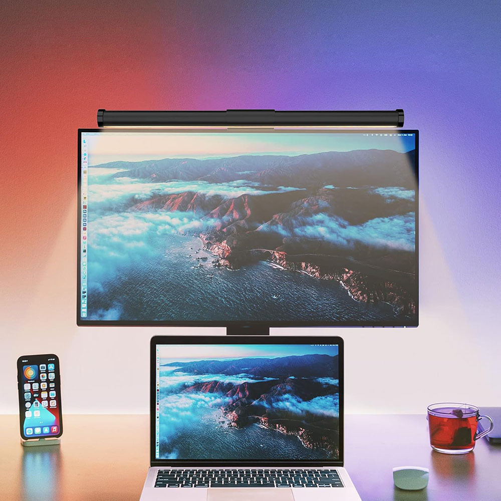 Una scrivania con monitor, laptop, telefono e tè. Il monitor mostra un paesaggio. Una barra luminosa è sopra il monitor.