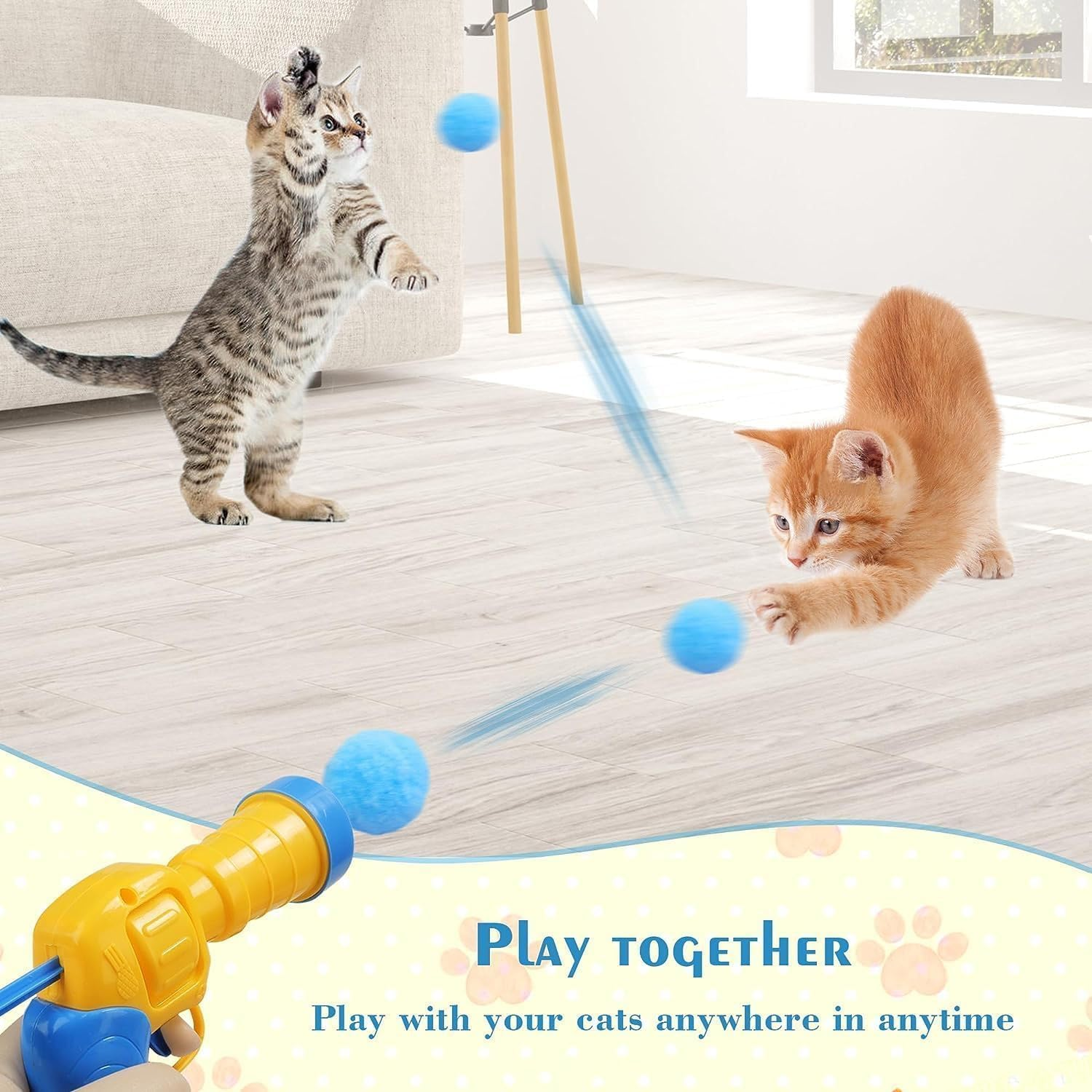 Zwei Kätzchen spielen mit blauen Bällen. Eine Katze steht, eine andere greift. Eine Spielzeugpistole ist im Vordergrund.