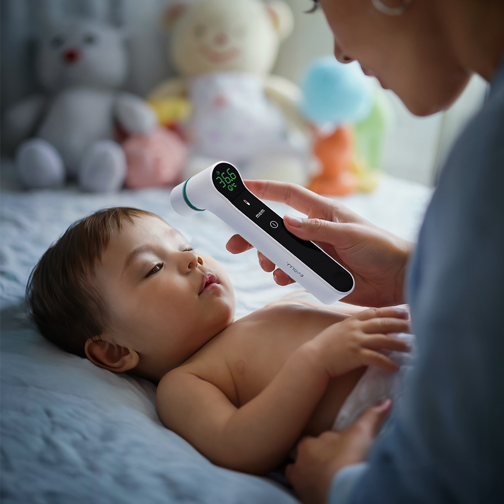 Eine Person benutzt ein Thermometer an einem Baby. Das Thermometer zeigt 36,6 Grad. Spielzeug ist im Hintergrund.