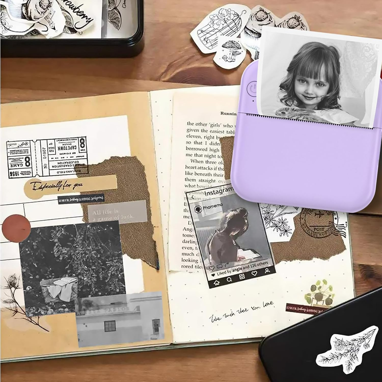 Ein Scrapbook mit Fotos, Aufklebern und einem kleinen Drucker. Ein Mädchenfoto wird gedruckt. Die Szene ist auf einem Holztisch.