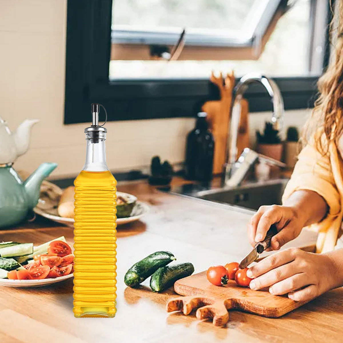 Eine Küchenszene mit einer Ölflasche, Gemüse und einer Person, die Tomaten auf einem Holzbrett schneidet. Der Hintergrund zeigt ein Waschbecken.