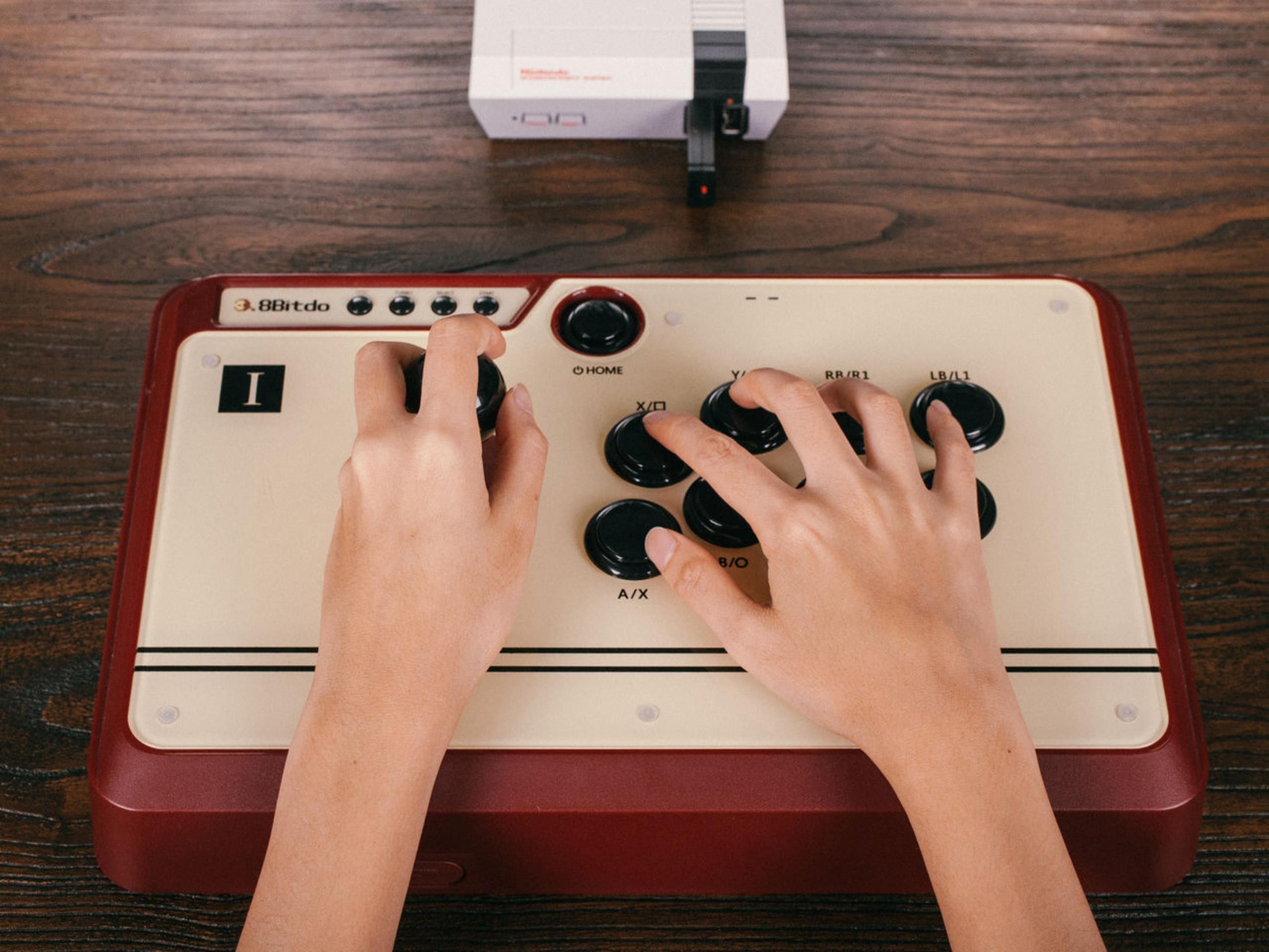 Mani su un controller di gioco retrò, con pulsanti e un joystick. Una console NES sullo sfondo.