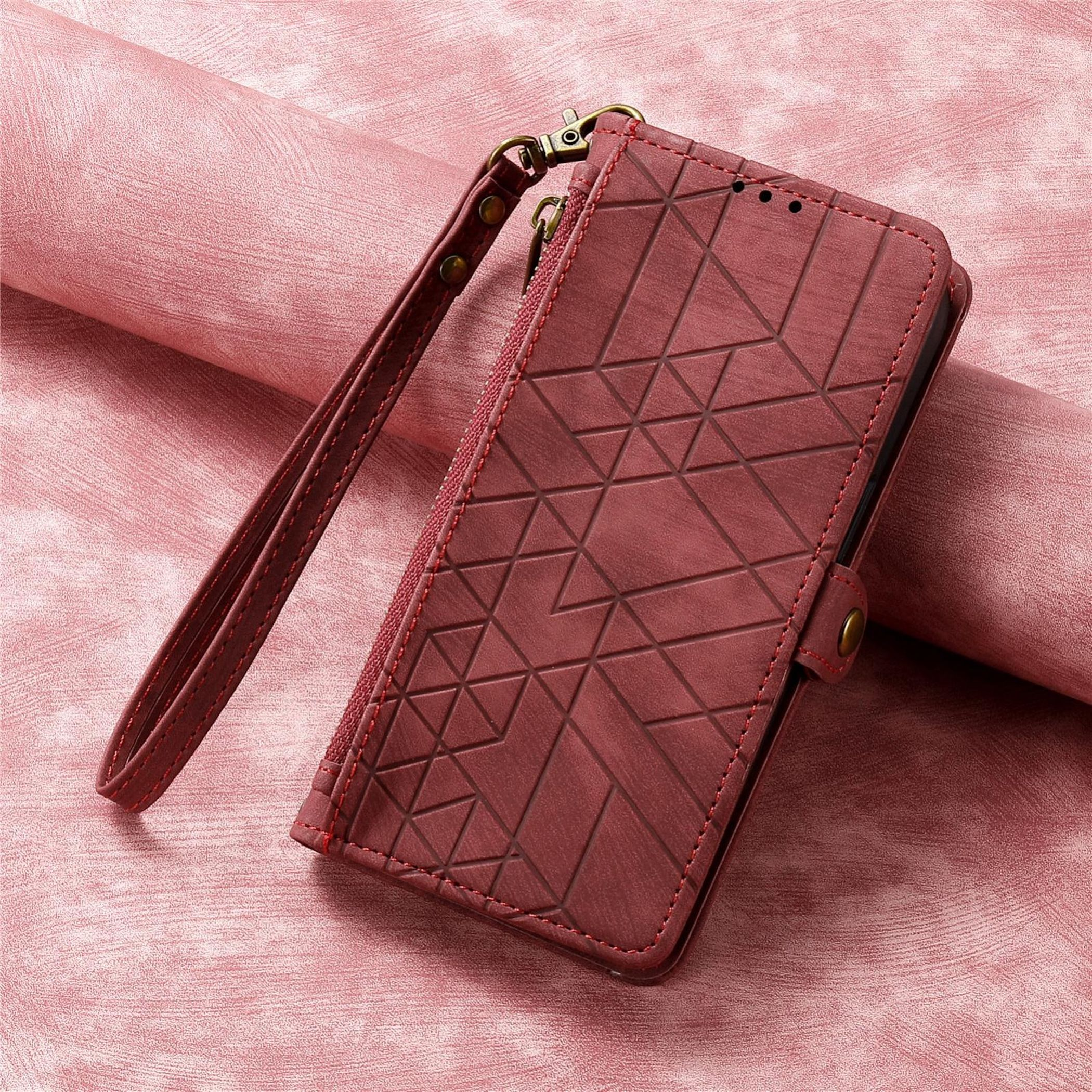 Eine weinrote Handyhülle mit Handschlaufe liegt auf einer rosa Oberfläche. Die Hülle hat ein geometrisches Muster und rote Nähte.