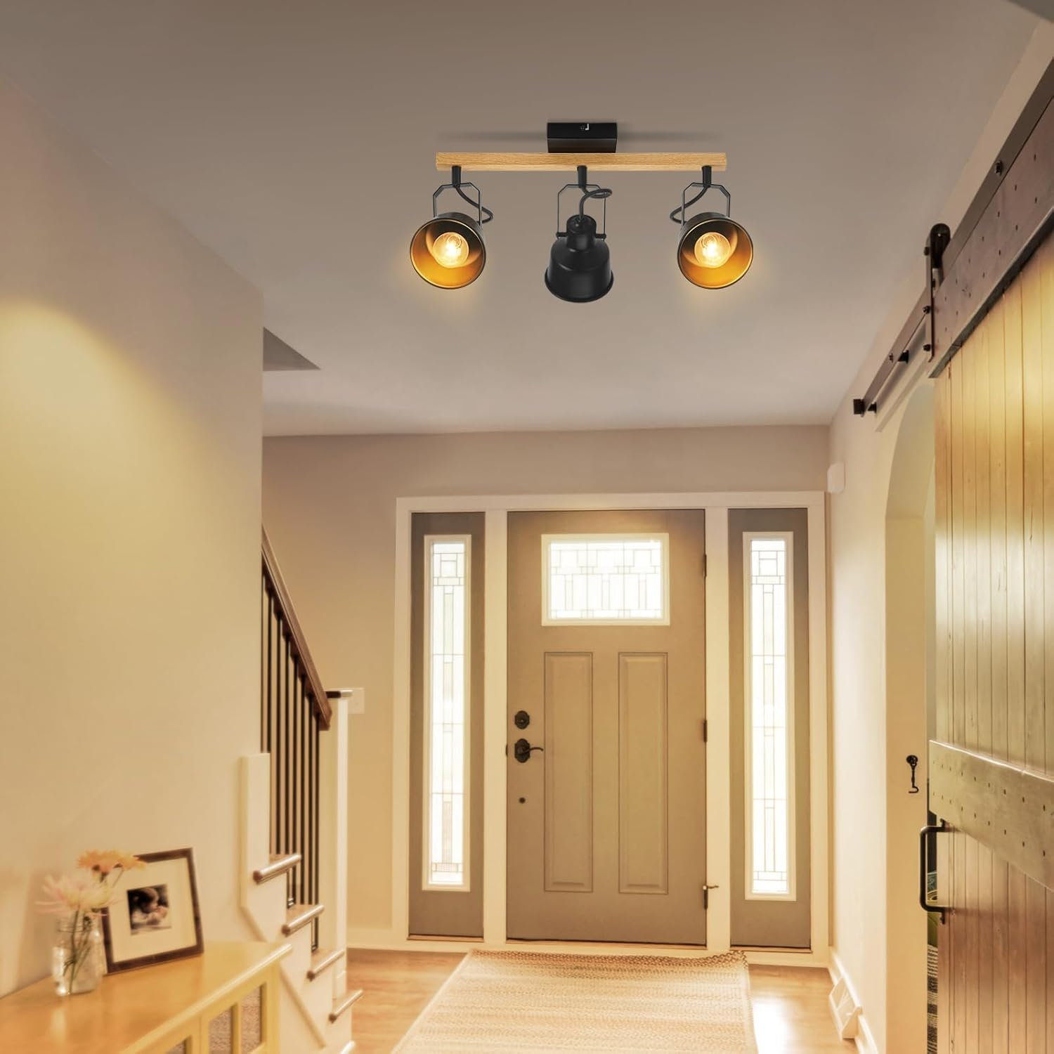 Korytarz z oświetleniem sufitowym. Widoczne drzwi i schody. Jasne ściany, drewniane drzwi. Ramka i kwiaty na stole.