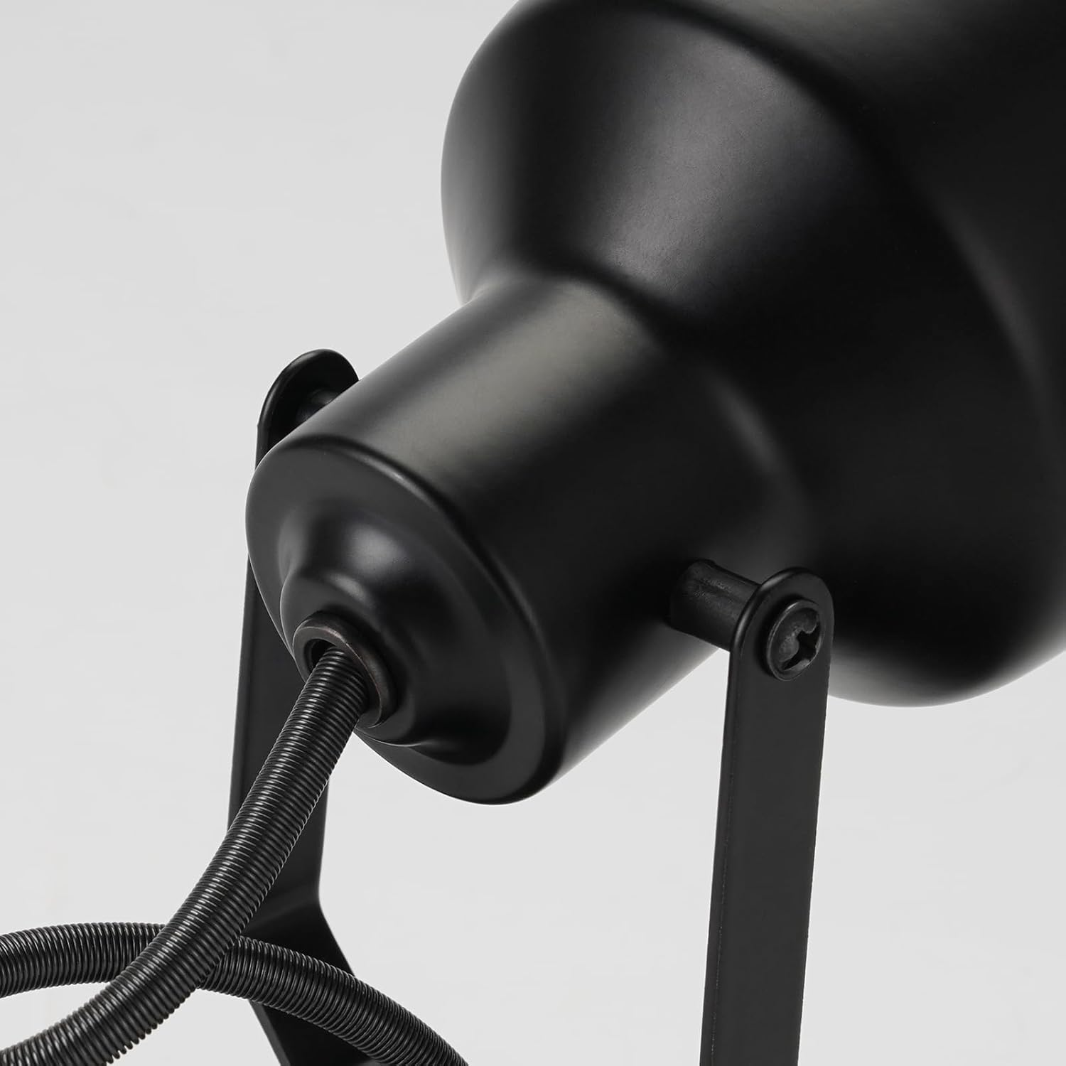 Zbliżenie czarnej lampy biurkowej, z elastycznym przewodem i ramą podtrzymującą na białym tle. Lampa jest skierowana w dół.