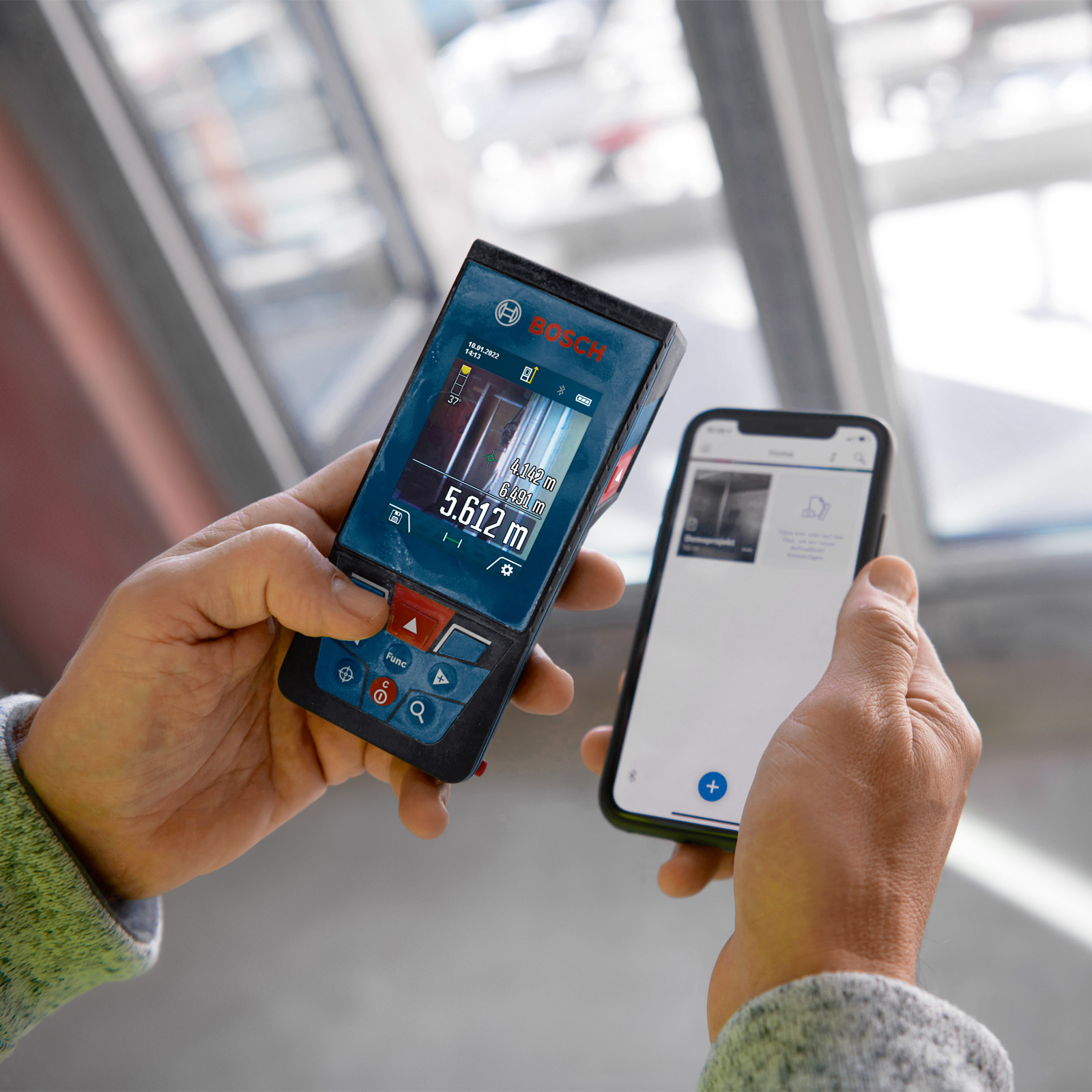 Bir kişi bir Bosch lazer ölçer ve bir akıllı telefon tutuyor. Ölçer ölçüm verilerini gösteriyor.