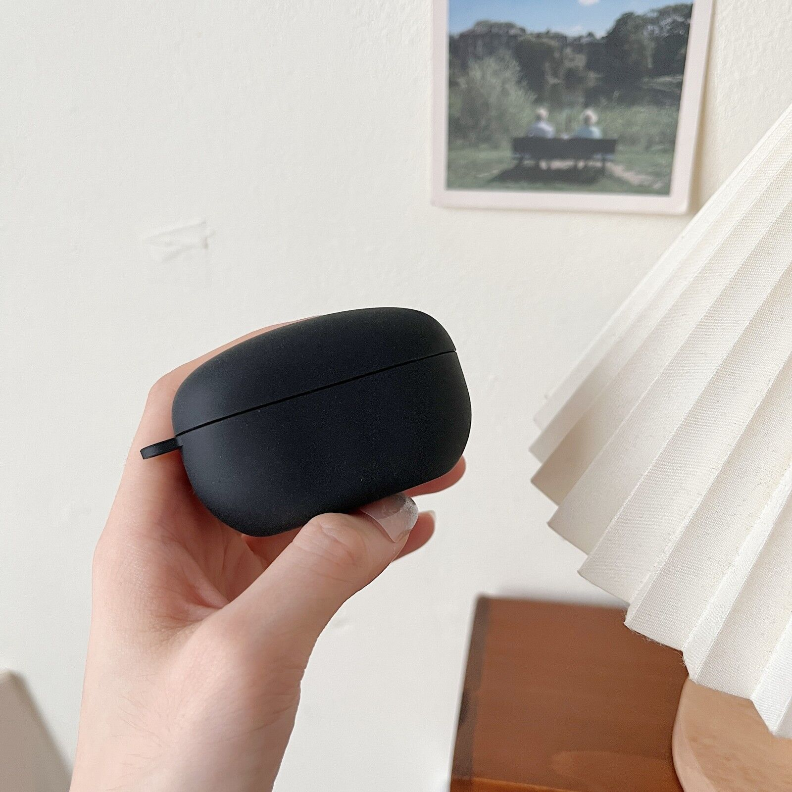 Eine Hand hält eine schwarze Kopfhörerhülle. Im Hintergrund ist ein Bild von Leuten auf einer Bank zu sehen.