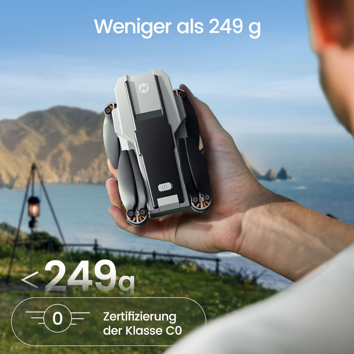 Eine Person hält eine Drohne. Sie ist weiß und schwarz mit orangefarbenen Propellern. Der Hintergrund zeigt Meer und Text mit Gewicht.