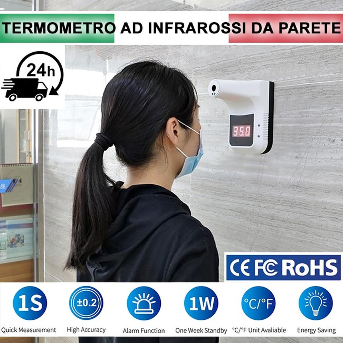 Una donna con la mascherina è in piedi vicino a un termometro a infrarossi a parete. Il termometro visualizza una temperatura.