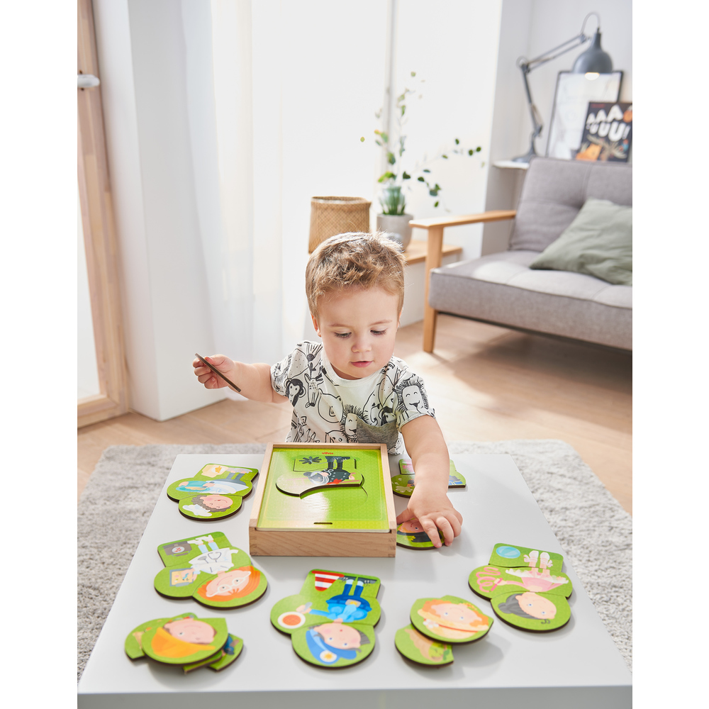 Małe dziecko bawi się puzzlami na białym stole. Puzzle mają zielone elementy i drewnianą ramę. Dziecko jest skupione.