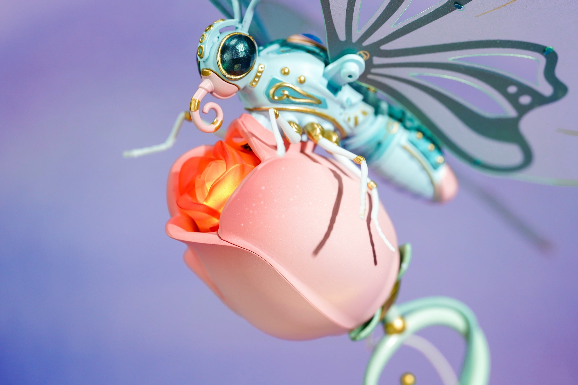 Fantastyczne stworzenie podobne do motyla na różowej róży. Stworzenie ma jasnoniebieskie i złote detale. Tło jest fioletowe.