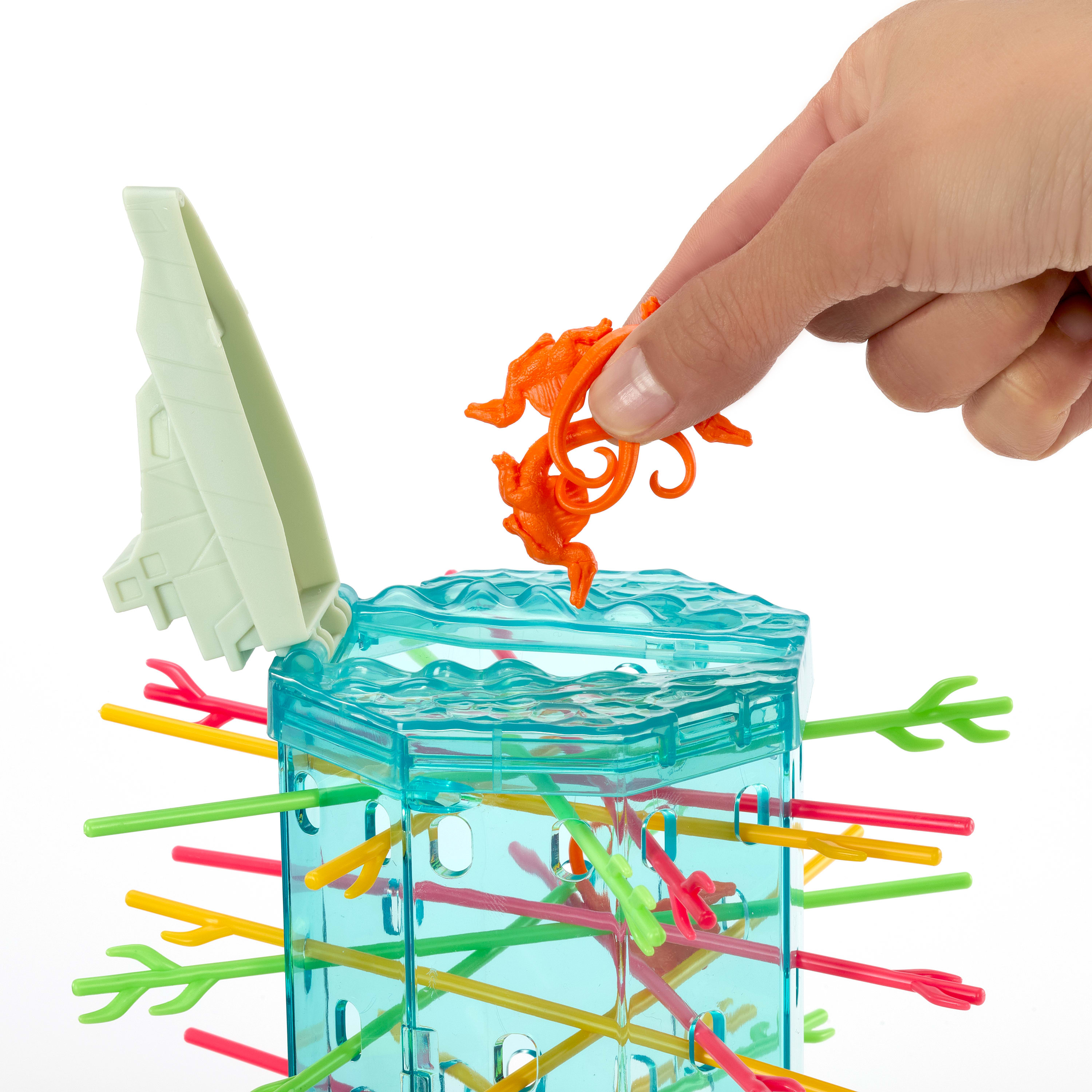 Une main place un jouet orange dans un jeu en plastique transparent avec des bâtons colorés. Le jeu est sur fond blanc.