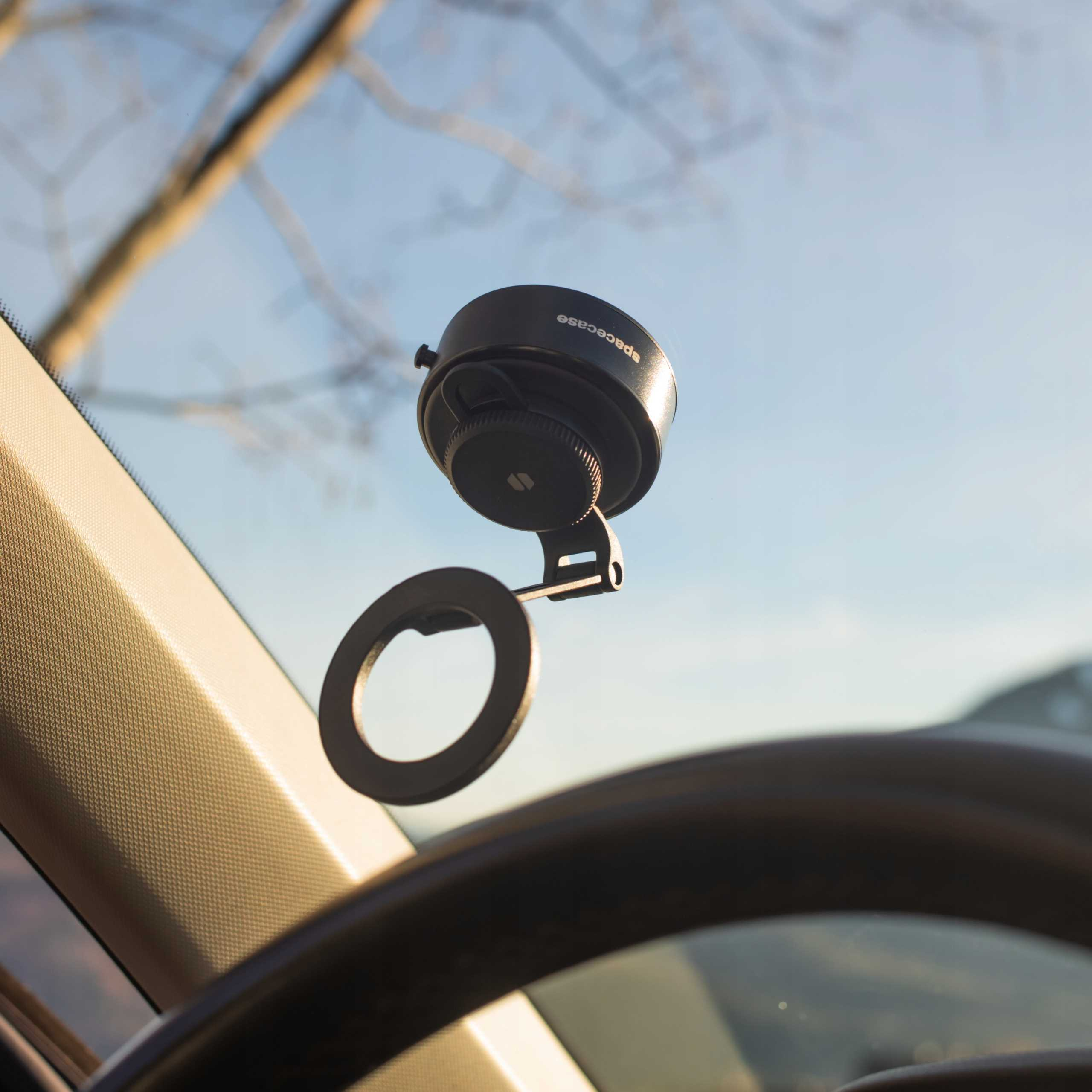 Uchwyt samochodowy na telefon z okrągłym uchwytem i przyssawką jest zamontowany na przedniej szybie, z kierownicą na pierwszym planie.