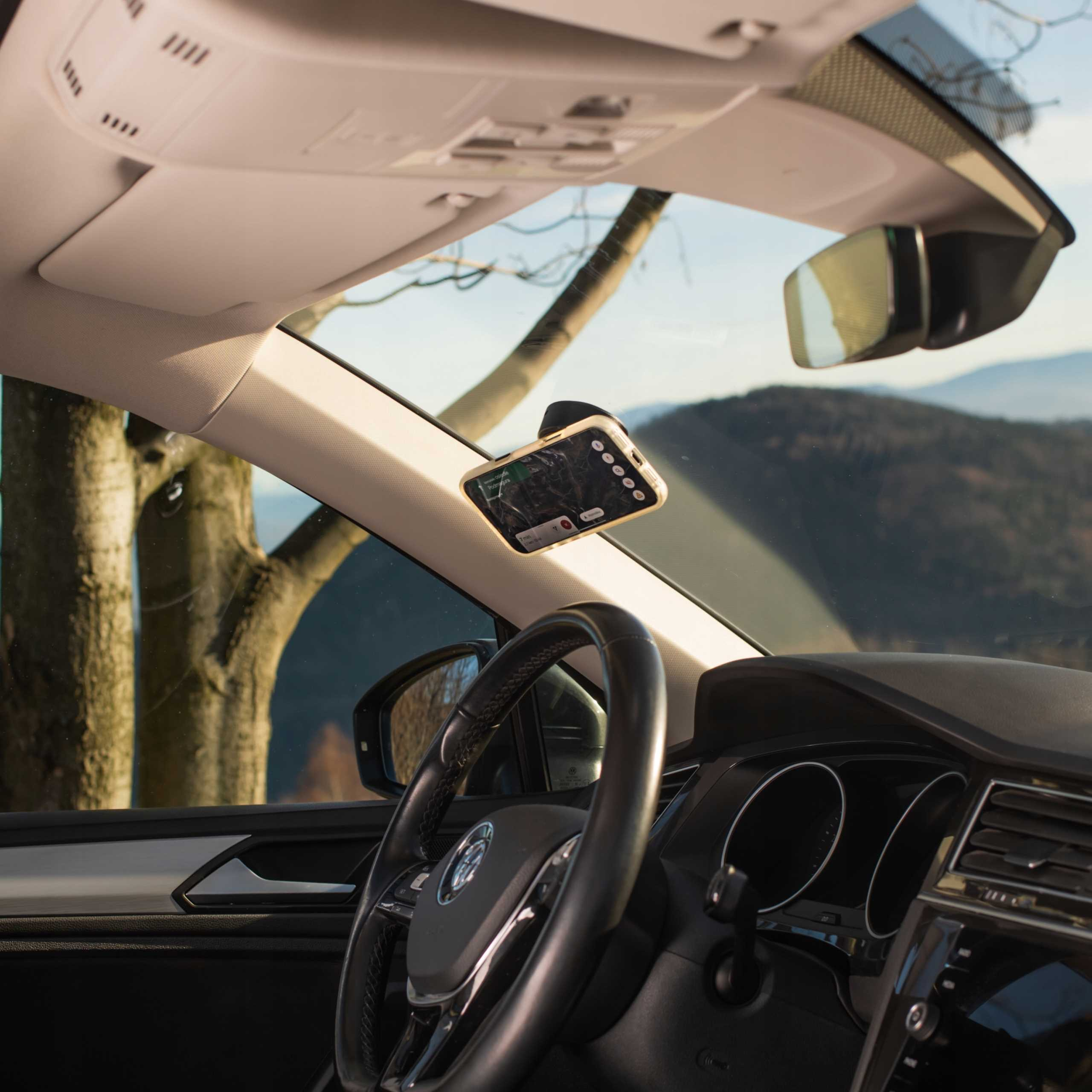 Wewnątrz samochodu telefon jest zamontowany na przedniej szybie. Widoczna jest kierownica i widok na drzewa i góry.