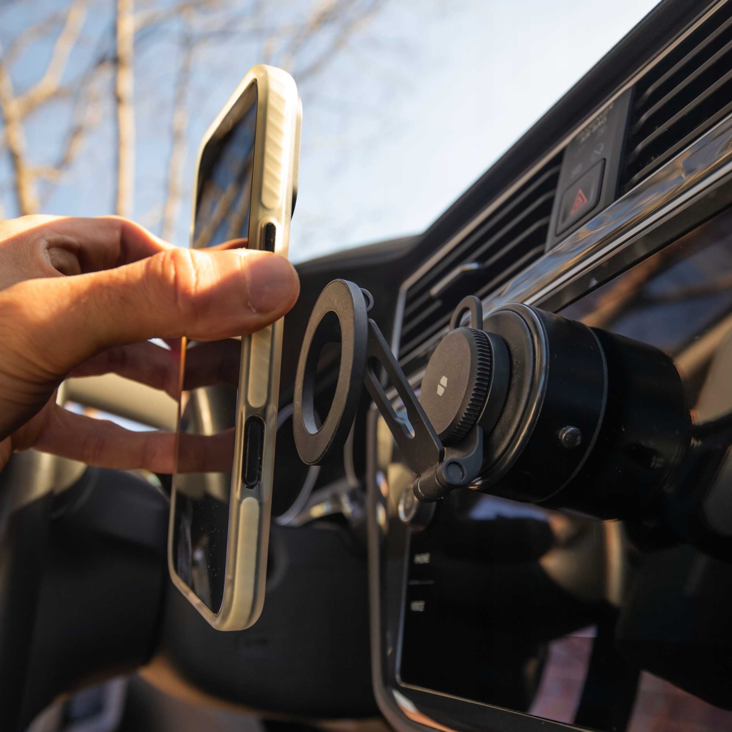 Ręka umieszcza telefon w uchwycie samochodowym. Telefon jest w etui. Scena dzieje się w samochodzie.