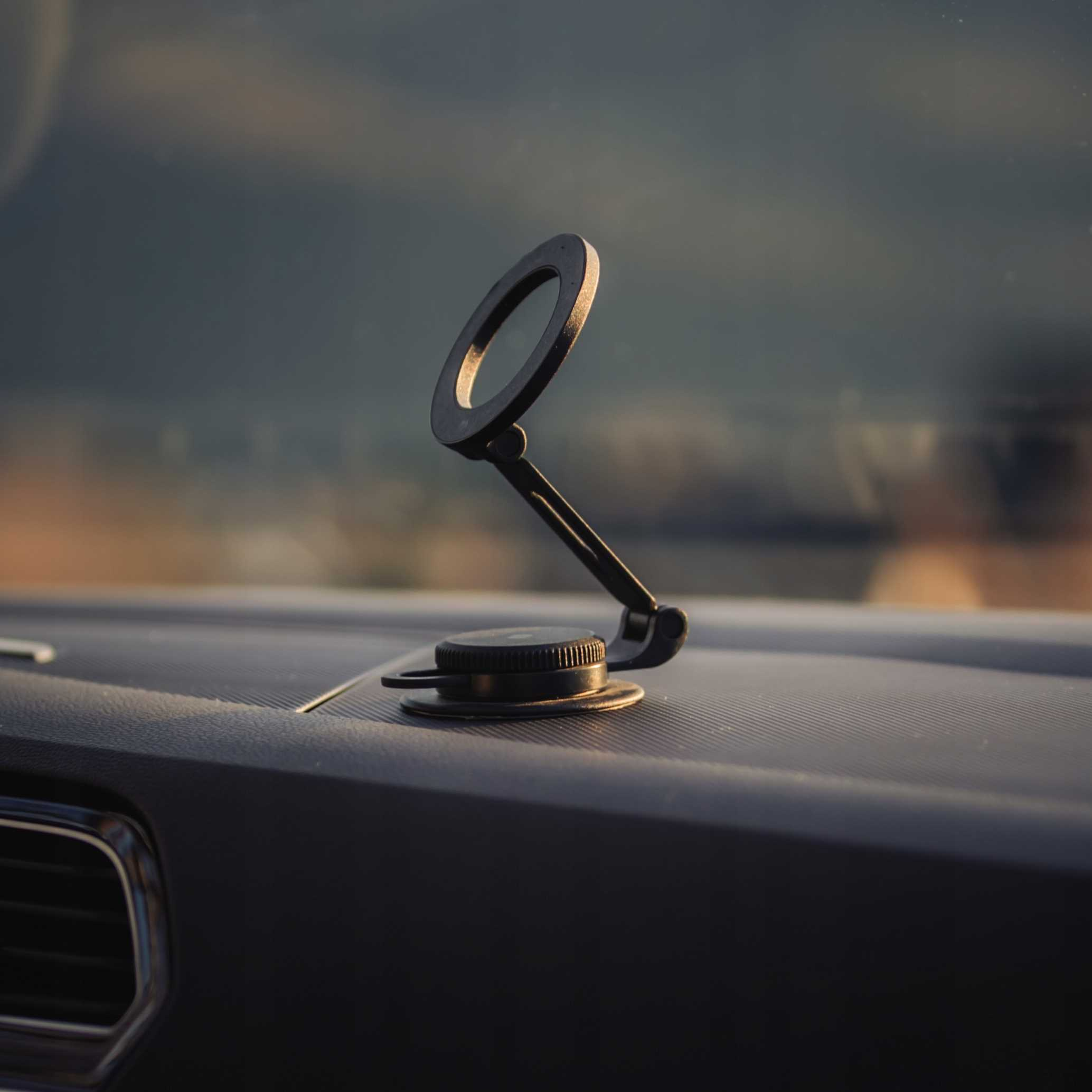 Czarny uchwyt na telefon jest zamontowany na desce rozdzielczej samochodu. Uchwyt ma pierścień i regulowane ramię.