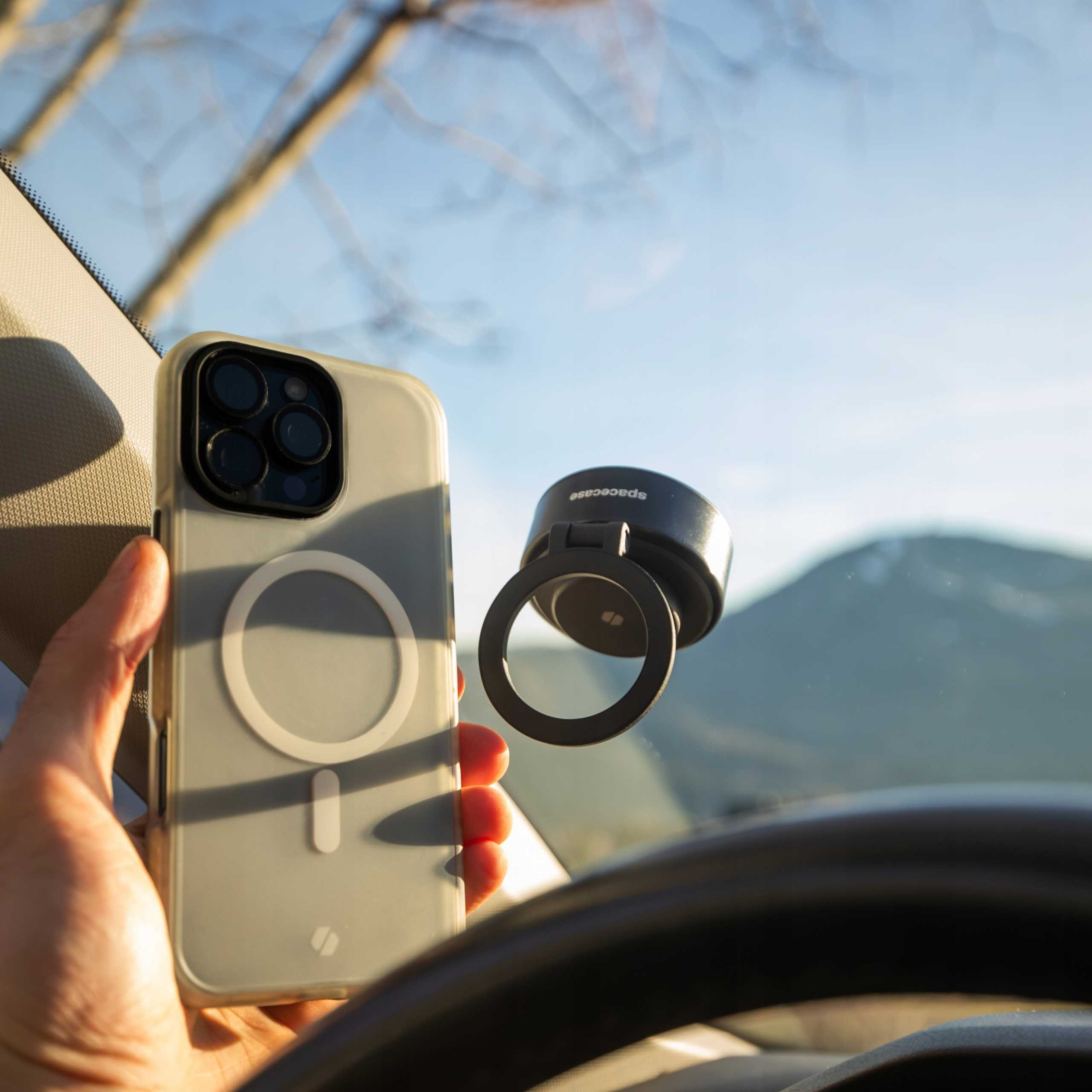 Dłoń trzymająca telefon z etui, uchwyt do telefonu na przedniej szybie, góry w tle.