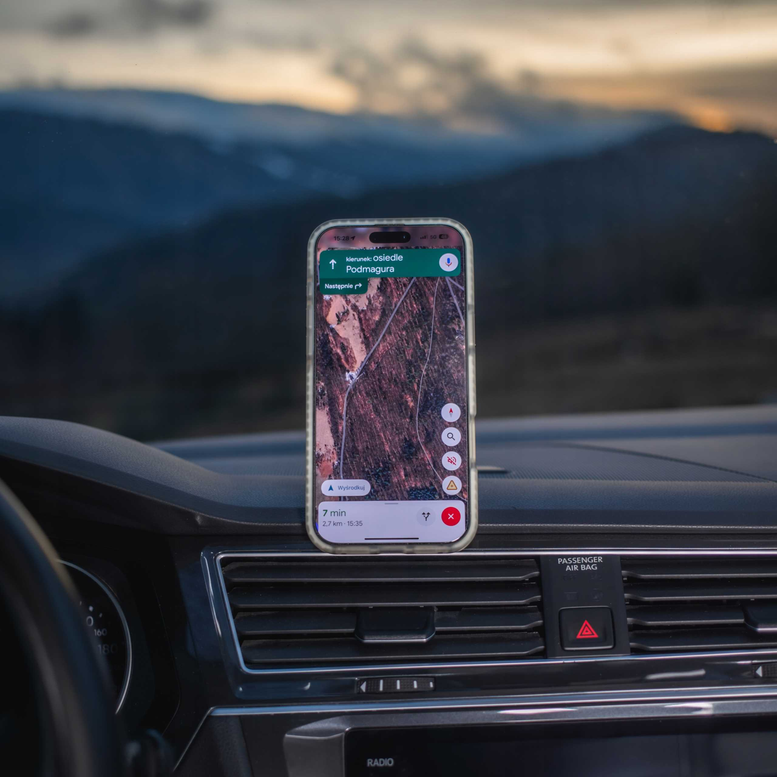 Telefon z mapą na desce rozdzielczej samochodu, w tle góry. Telefon pokazuje nawigację.