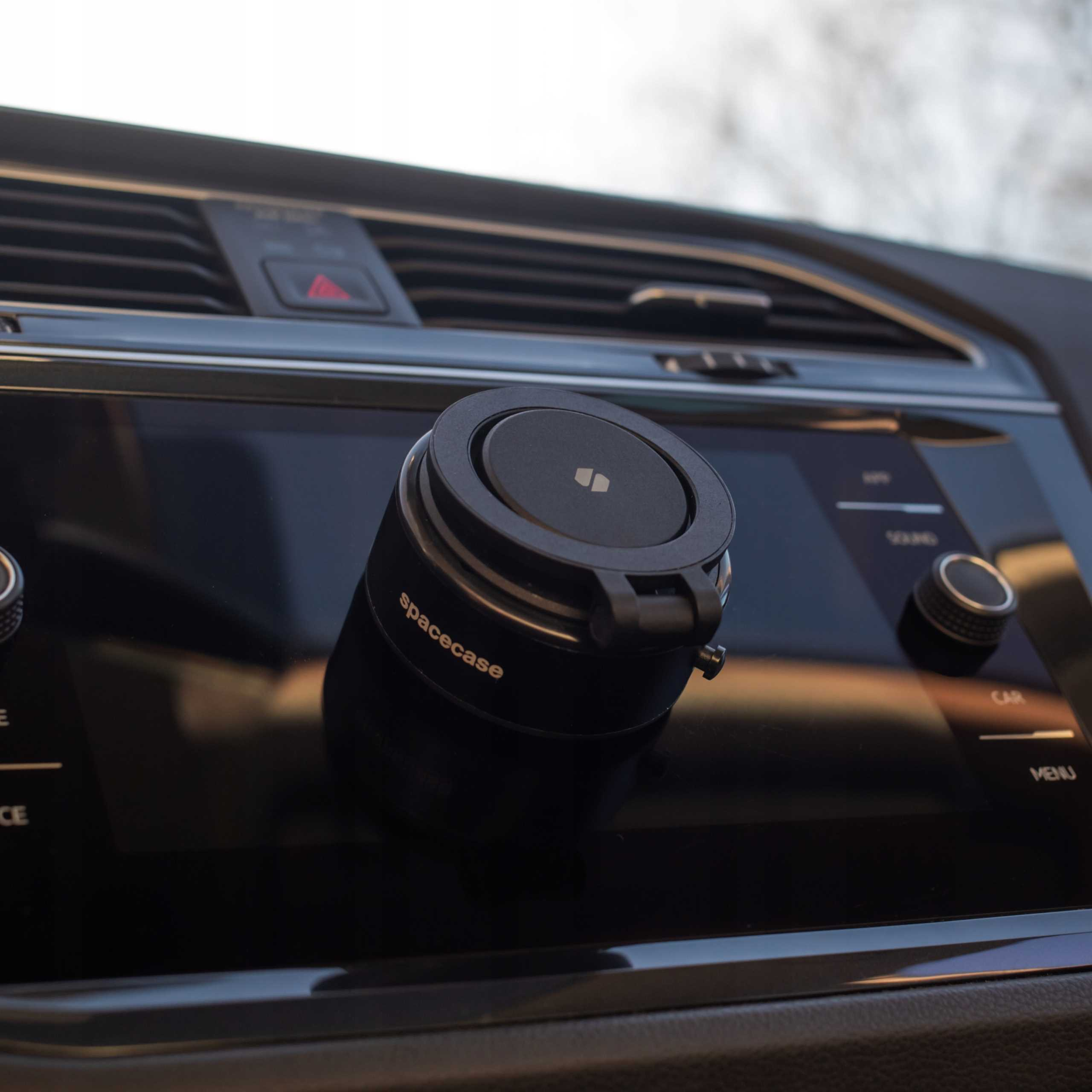 Czarne urządzenie Spacecase jest zamontowane na desce rozdzielczej samochodu. Wyświetlacz i elementy sterujące są widoczne. Tło rozmyte.