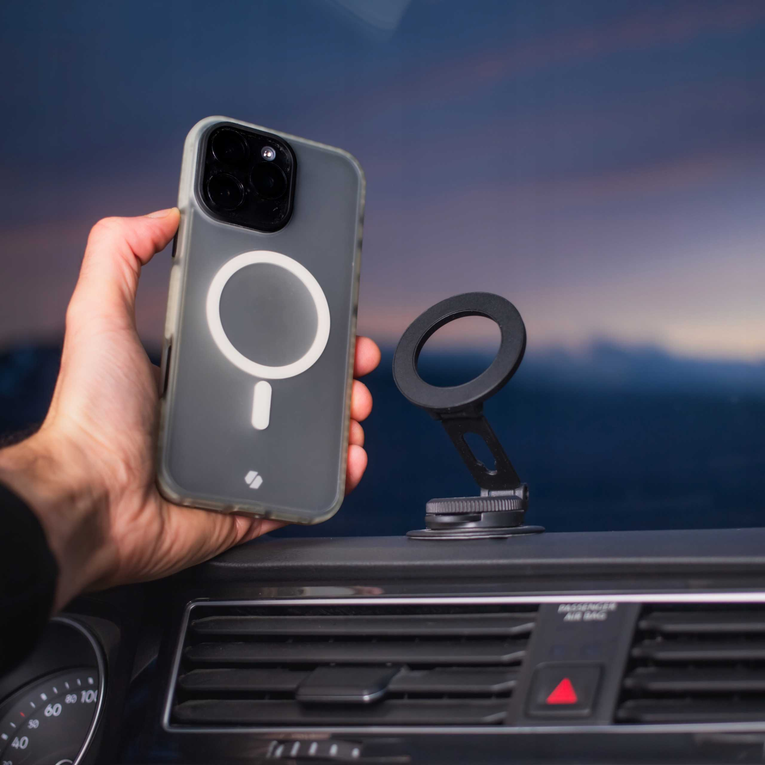 Ręka trzymająca telefon w etui z uchwytem samochodowym w samochodzie, niebieskie niebo w tle.