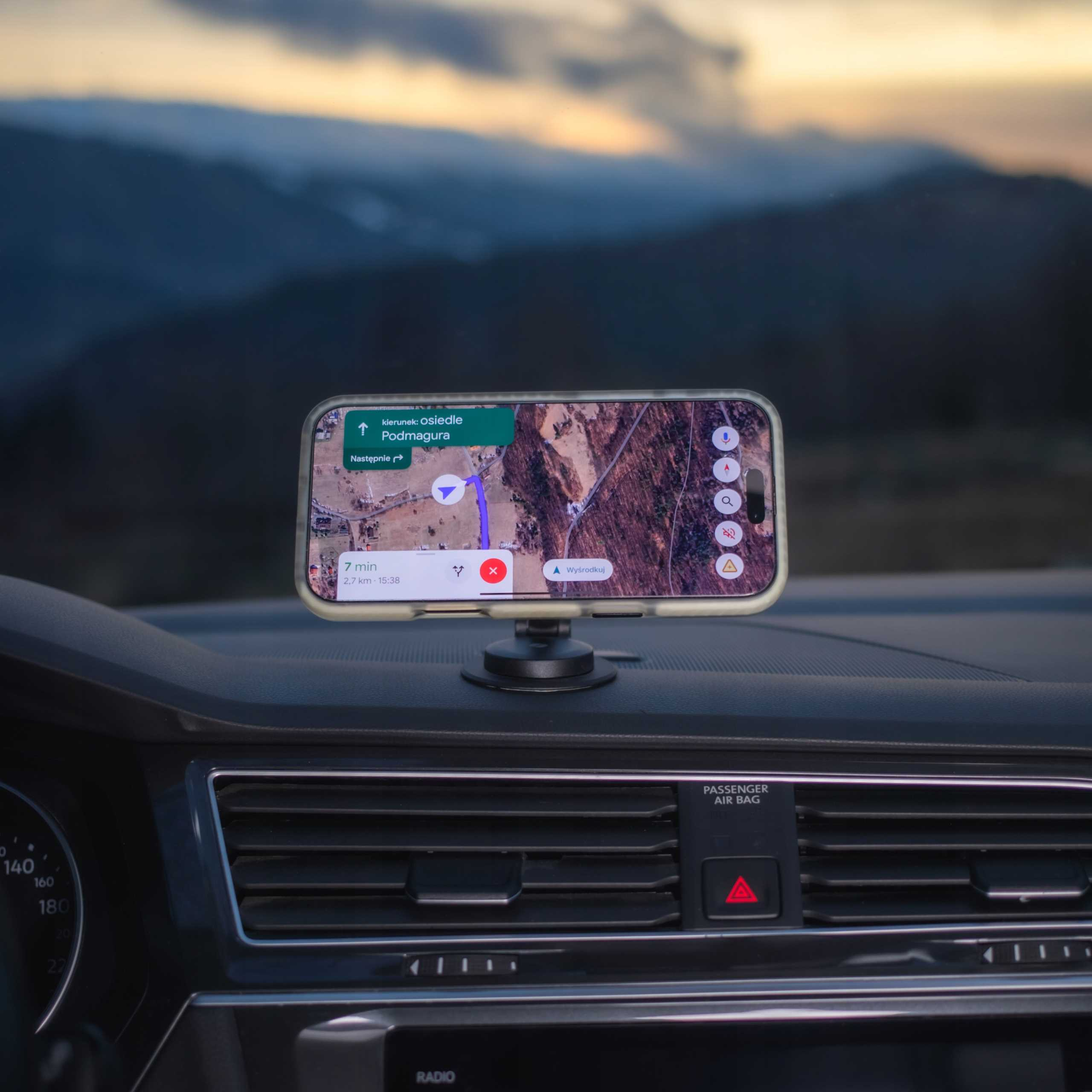 Telefon z nawigacją zamontowany na desce rozdzielczej samochodu, z rozmytym pasmem górskim w tle.