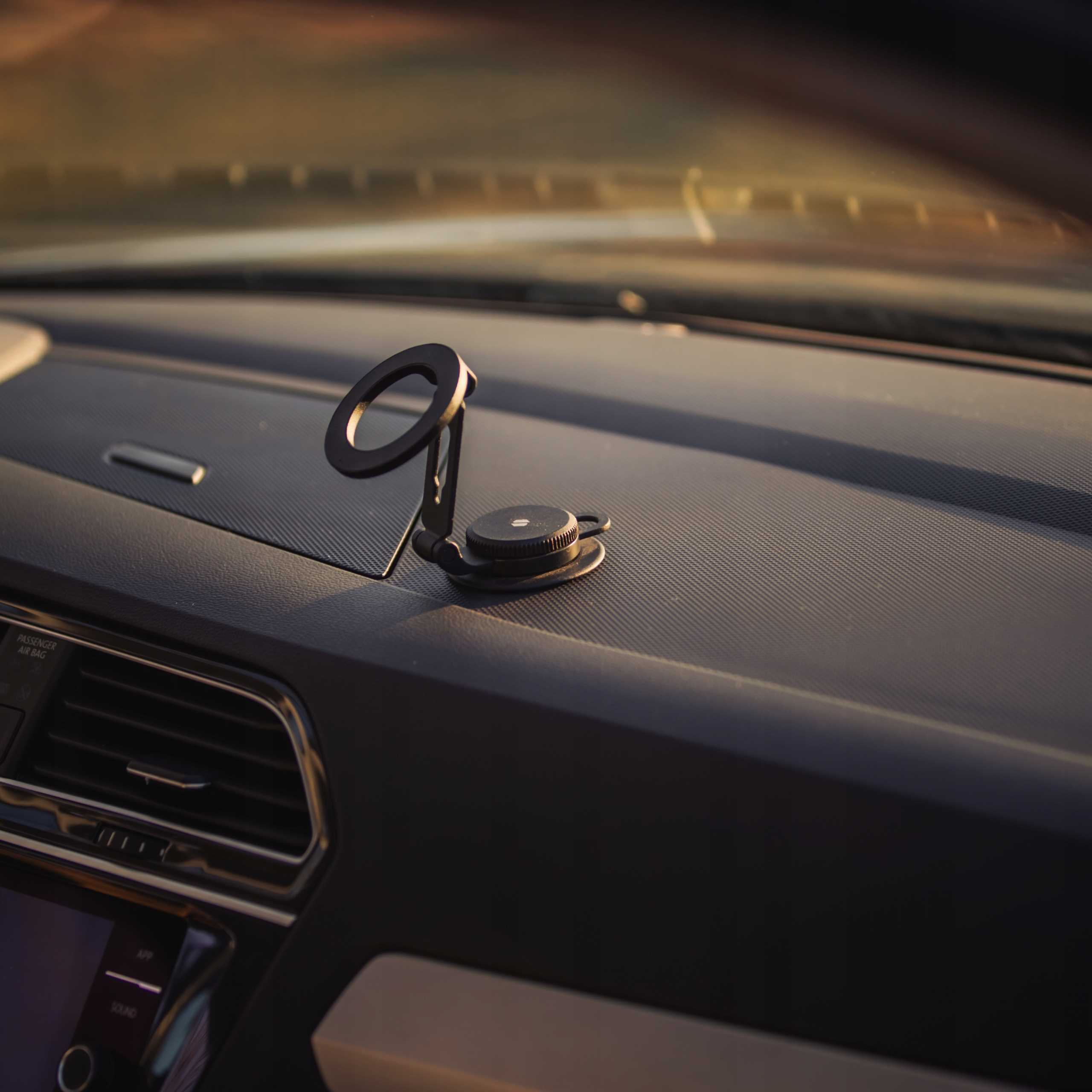 Deska rozdzielcza samochodu z uchwytem na telefon. Czarny uchwyt na desce rozdzielczej. Wnętrze samochodu. Oświetlenie zachodzącego słońca.