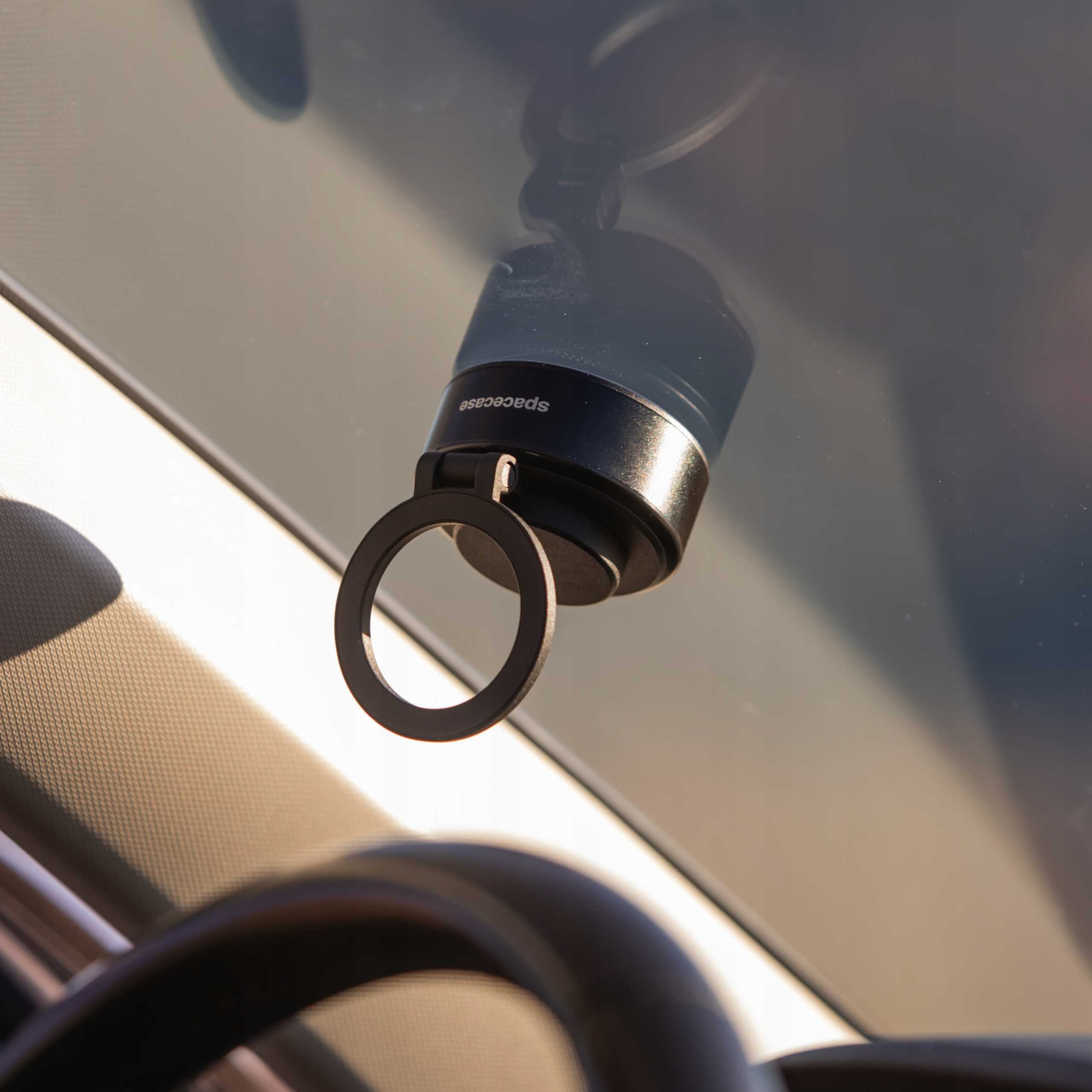 Czarne urządzenie jest przymocowane do szyby samochodowej. Ma pierścień z napisem 'spacecase'.