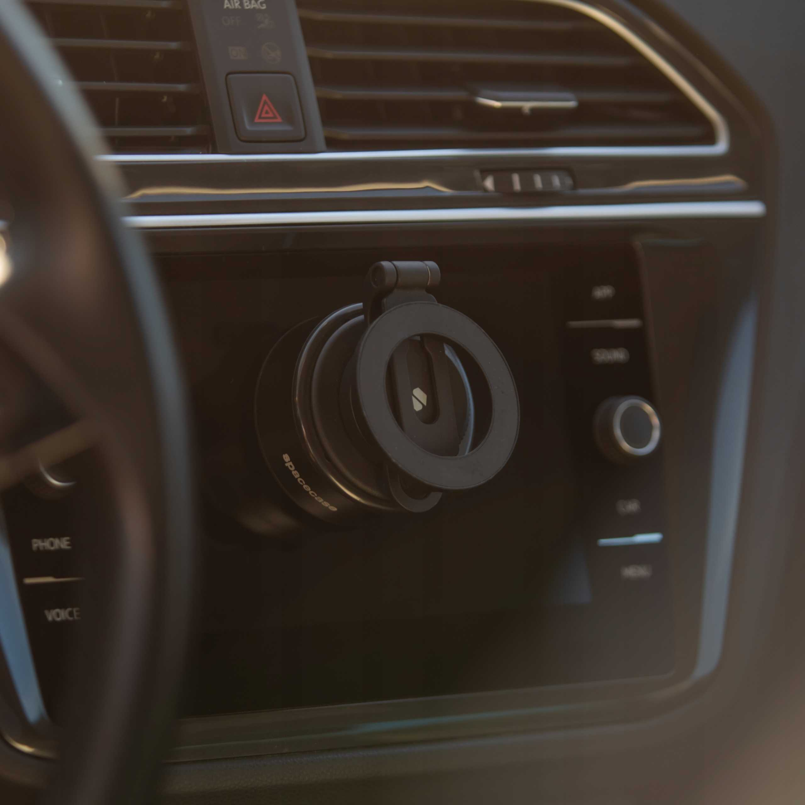 Deska rozdzielcza samochodu z uchwytem na telefon. Widoczny otwór wentylacyjny, przycisk awaryjny. Widoczne są również przyciski telefonu i głosu.