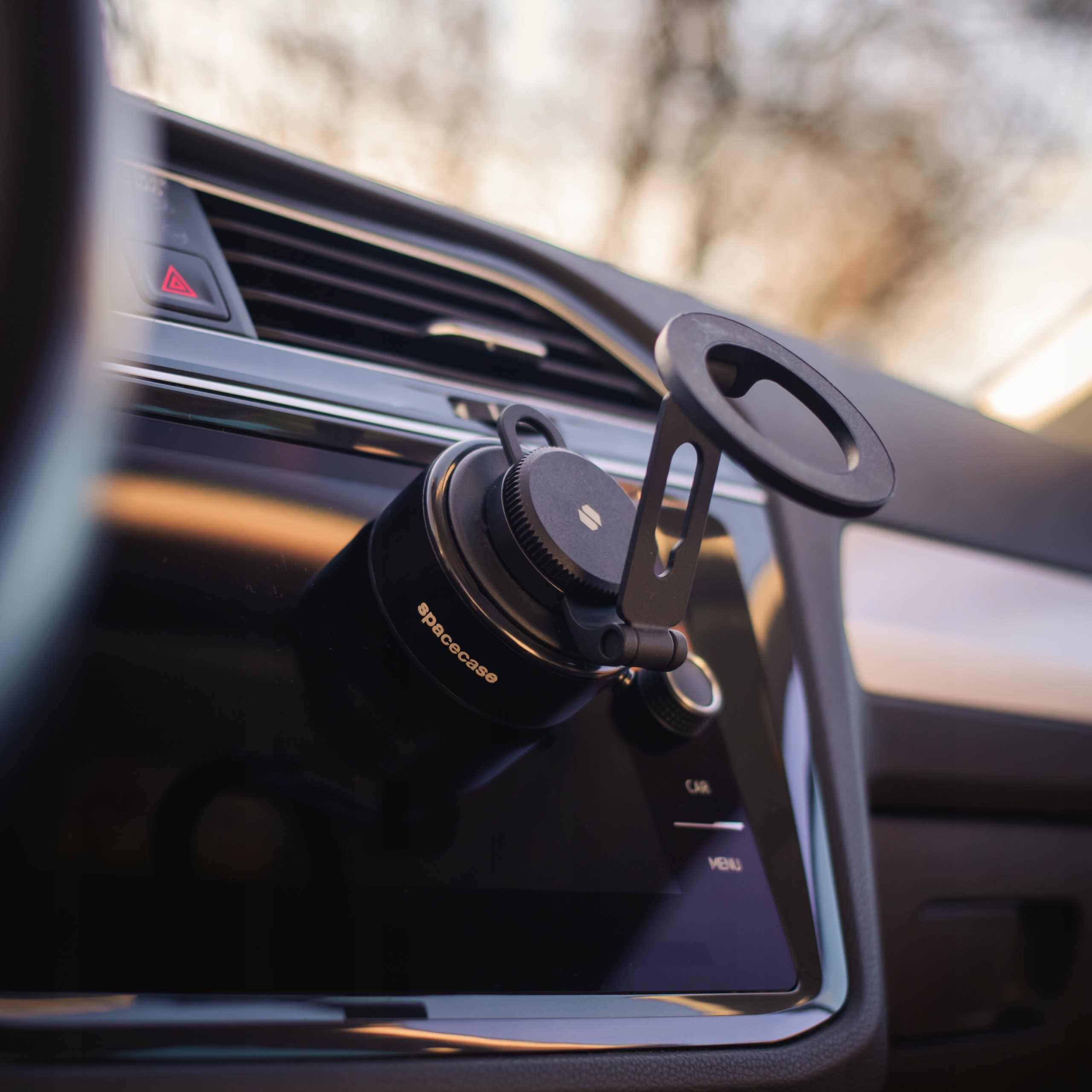 Wnętrze samochodu z czarnym uchwytem na telefon. Widoczny czerwony przycisk świateł awaryjnych. Na uchwycie napis 'spacecase'.