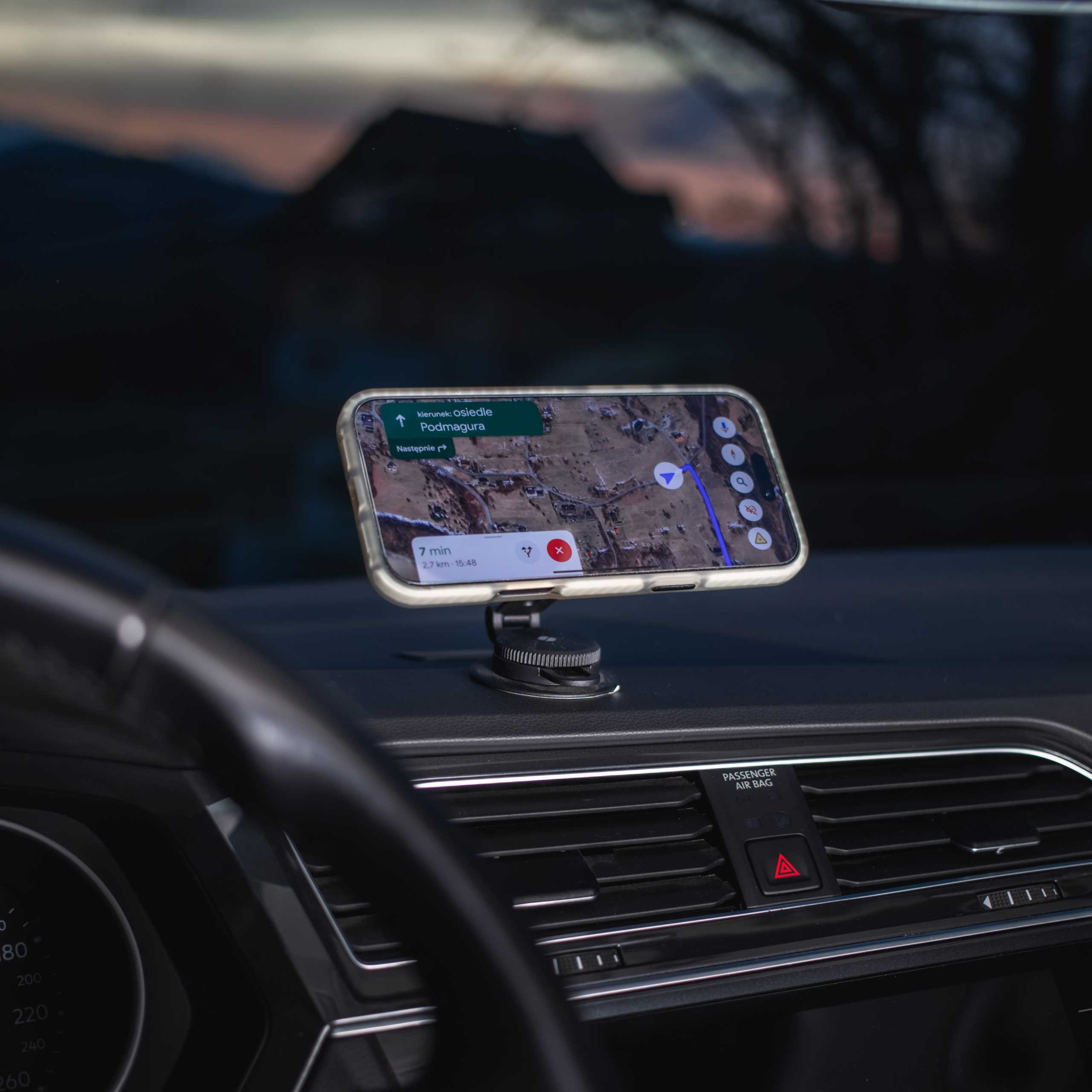 Telefon z mapą zamontowany w samochodzie. Widoczna deska rozdzielcza i kierownica. W tle góry.