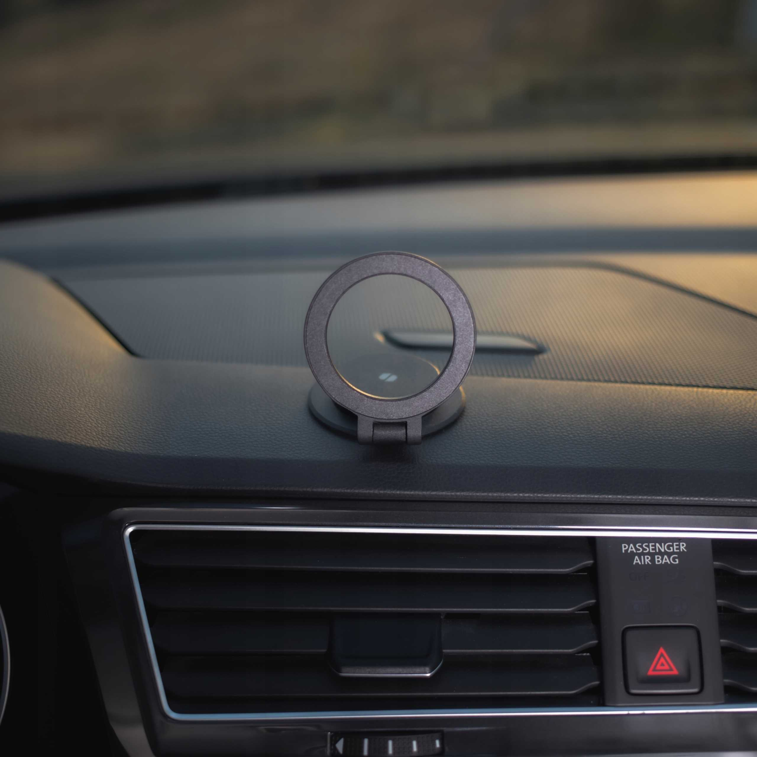 Deska rozdzielcza samochodu z okrągłym uchwytem na telefon. Widoczne kratki wentylacyjne i przycisk świateł awaryjnych.
