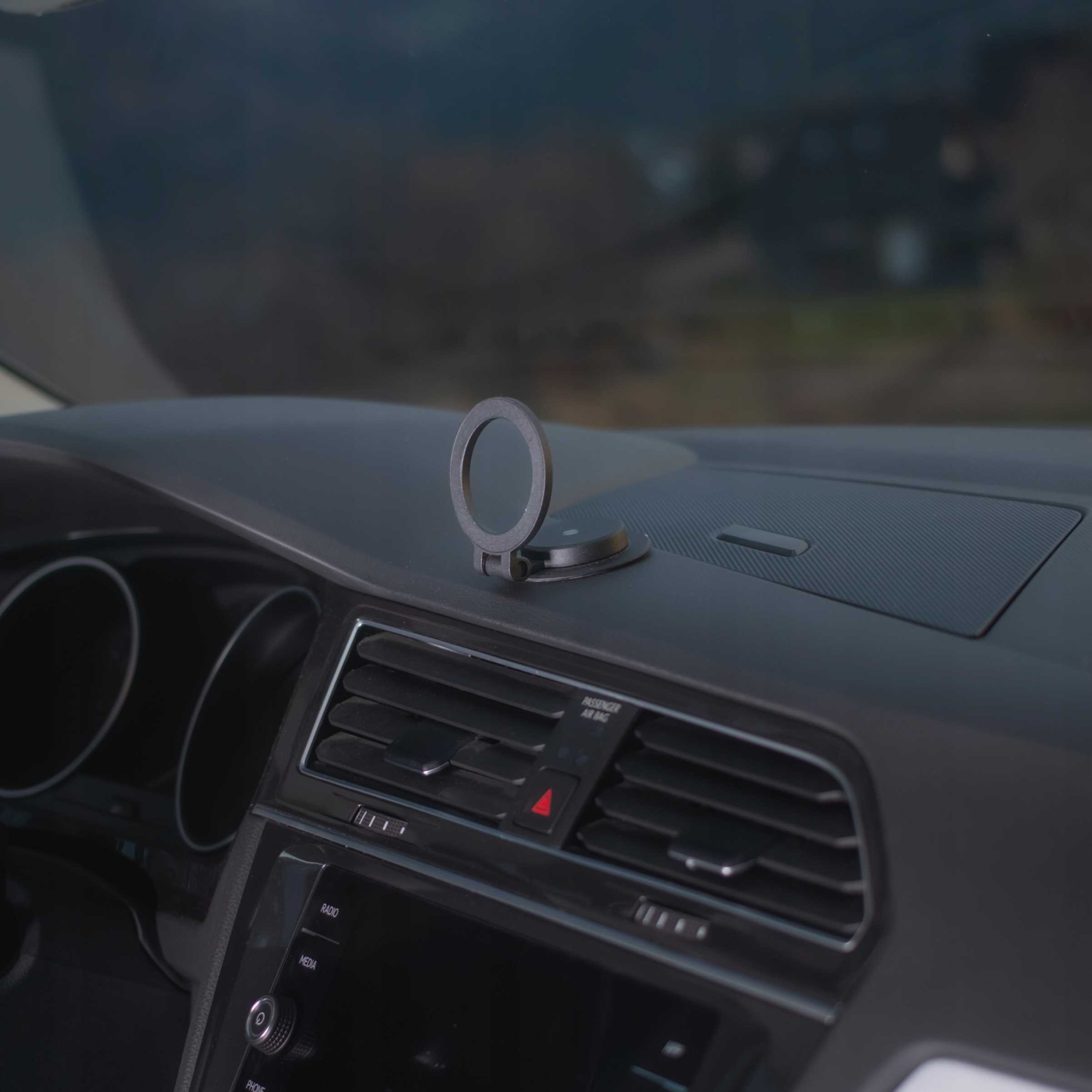 Deska rozdzielcza samochodu z uchwytem na telefon. Deska rozdzielcza jest czarna. Widoczny jest czerwony trójkąt. Tło jest rozmyte.