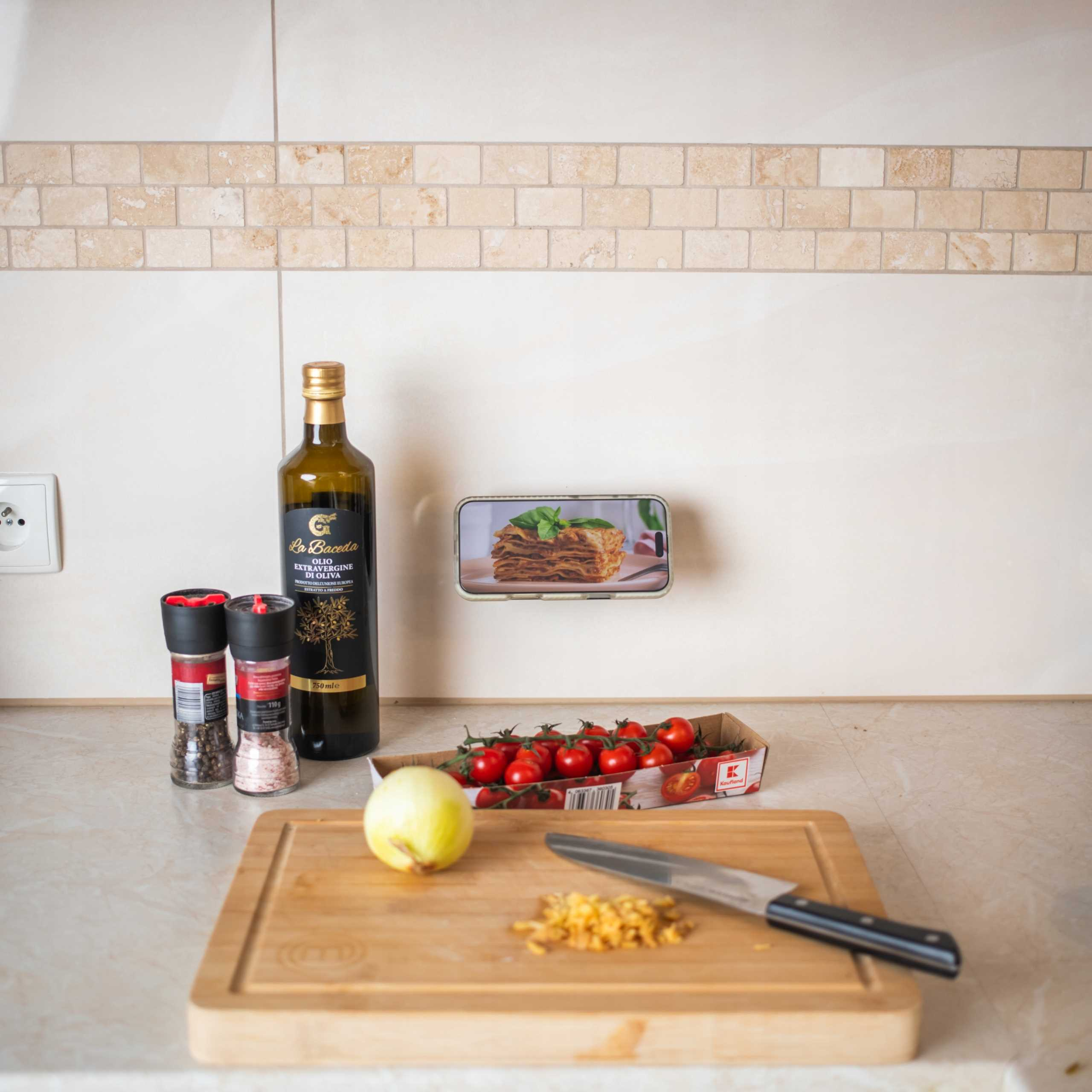 Scena kuchenna ze składnikami: oliwa z oliwek, pomidory, cebula, sól/pieprz i telefon z lasagną.