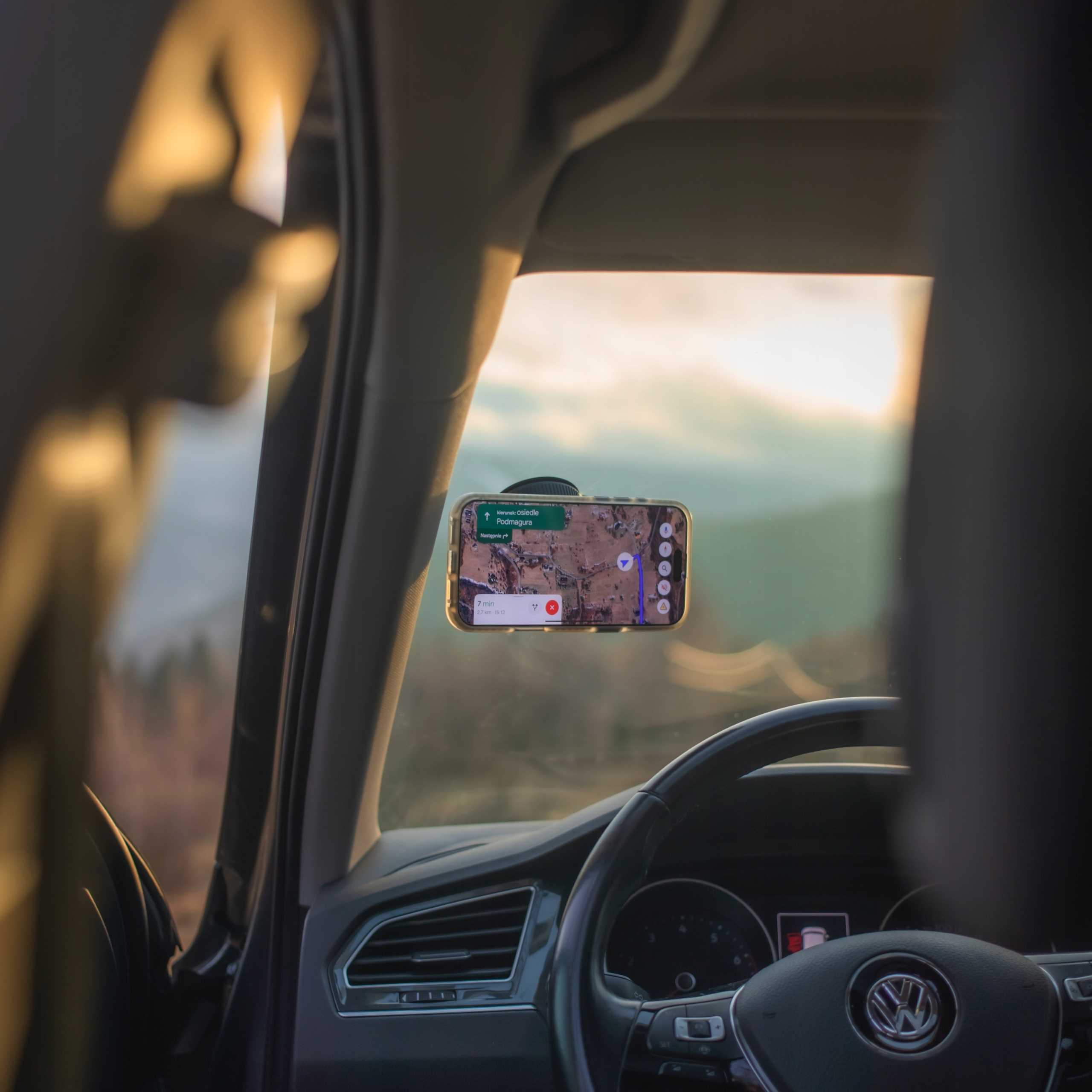 Telefon z mapą zamontowany w samochodzie. Widoczna kierownica i widok na zewnątrz.