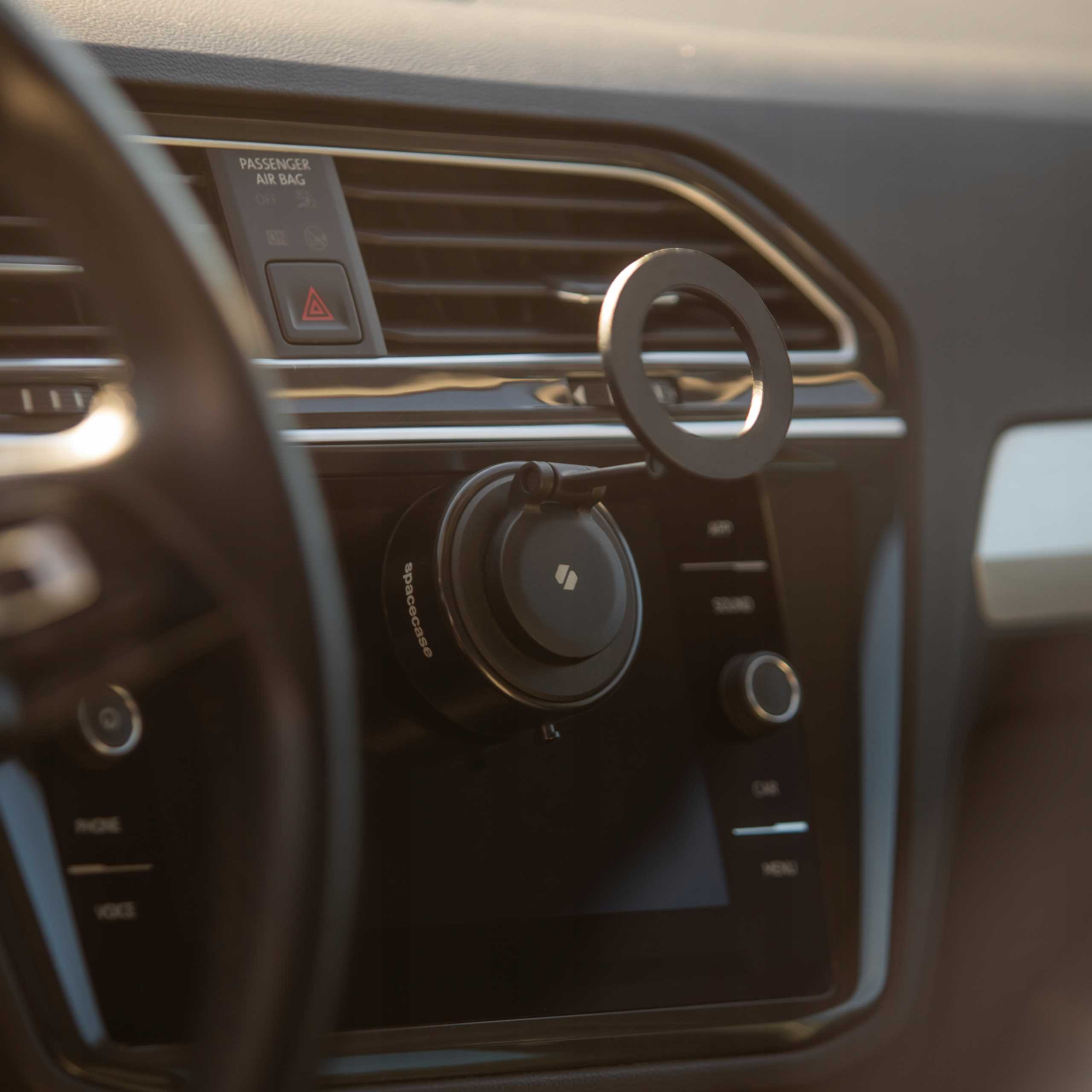 Wnętrze samochodu z uchwytem na telefon. Czarna deska rozdzielcza, kierownica i elementy sterowania samochodem. Widoczna poduszka powietrzna i światła awaryjne.