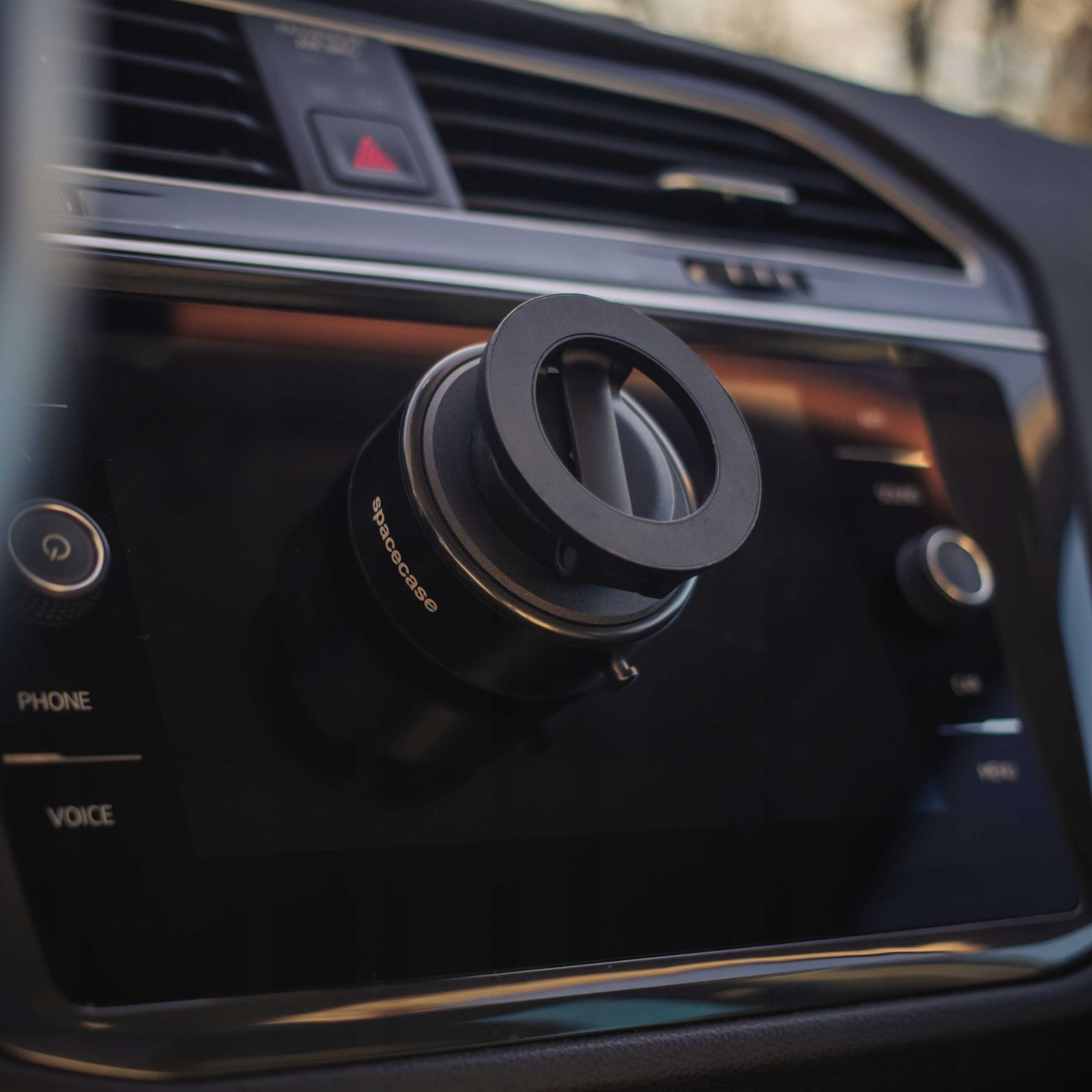 Czarne wnętrze samochodu z uchwytem na telefon na ekranie informacyjnym. Uchwyt jest okrągły, z logo.