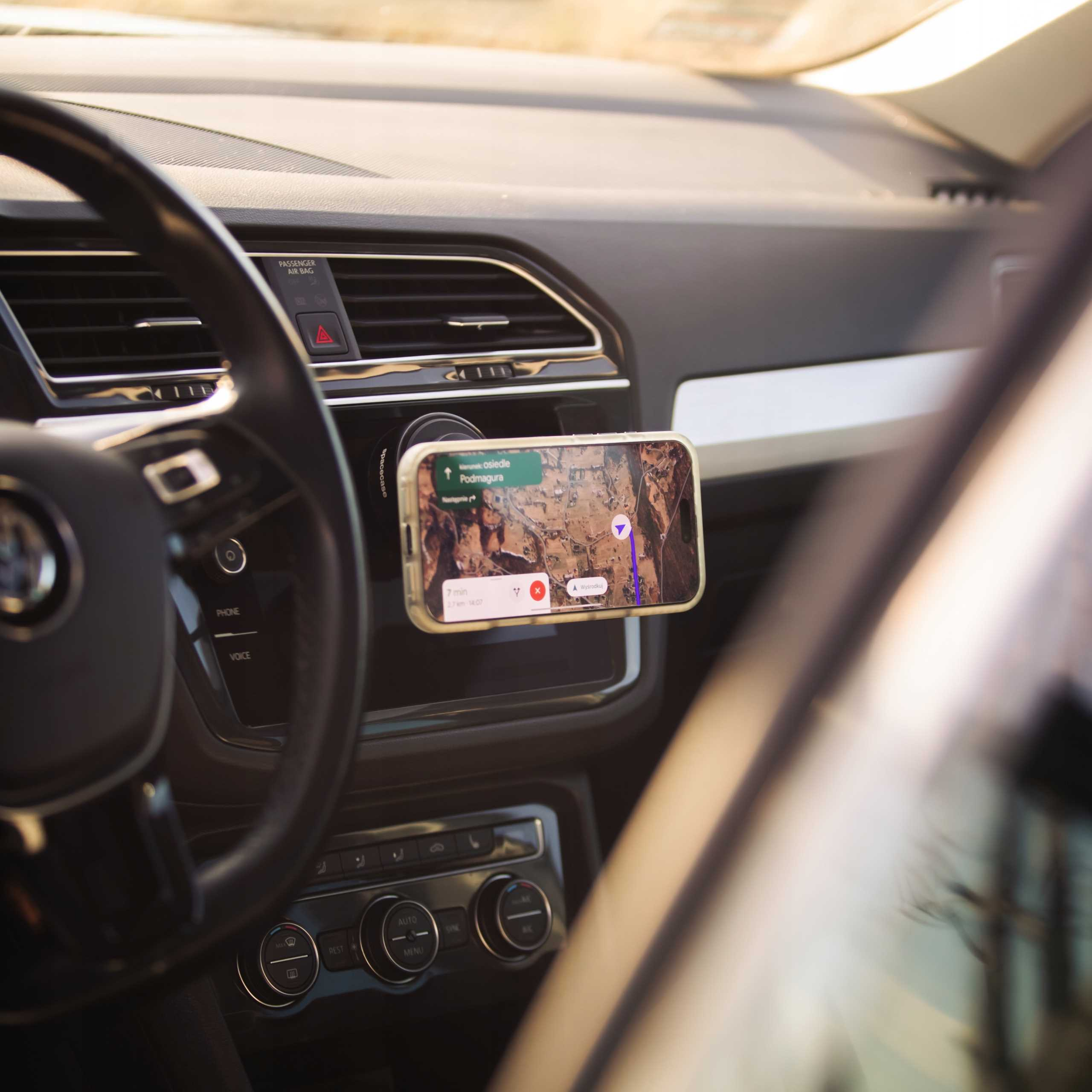 Telefon z mapą zamontowany na desce rozdzielczej samochodu. Widoczna kierownica i wnętrze samochodu.