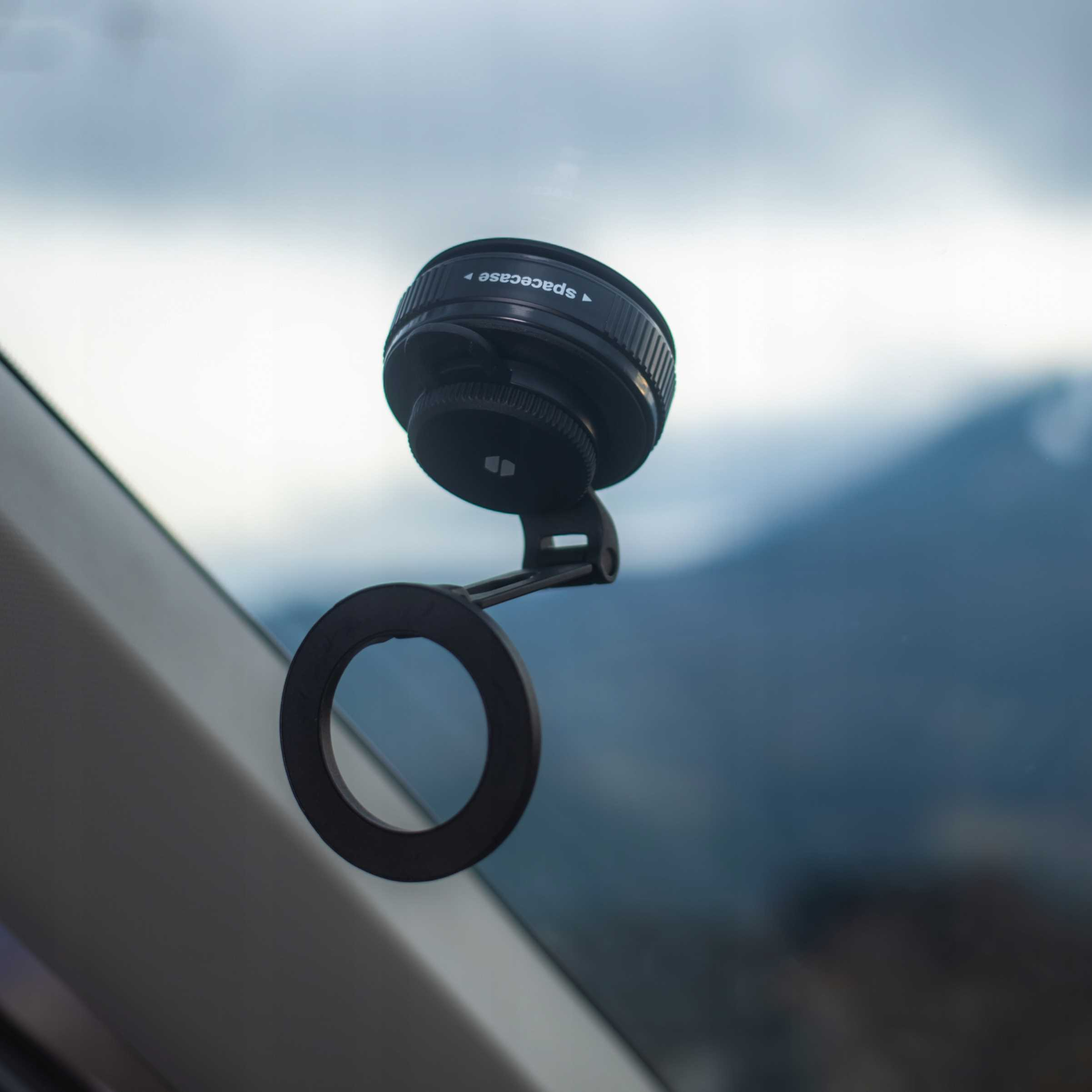 Czarny uchwyt do telefonu samochodowego jest przymocowany do szyby. Na tle widać niebo.