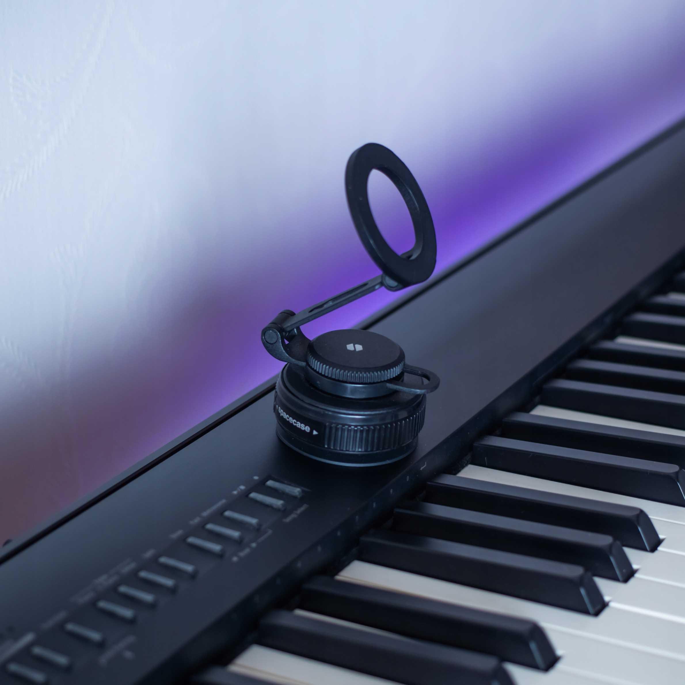 Czarna klawiatura z czarnym akcesorium na górze. Klawisze są czarno-białe. Fioletowe światło w tle.