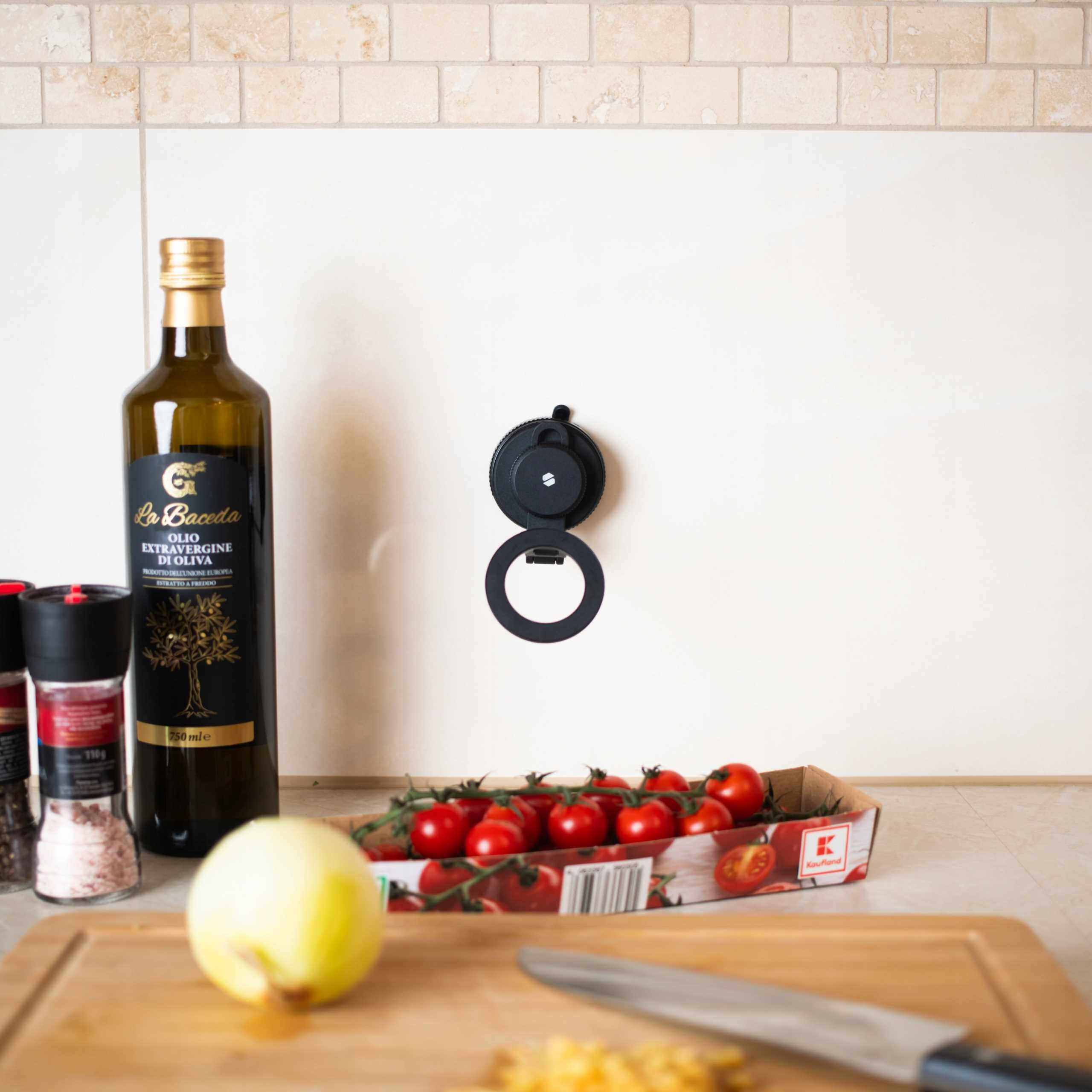 Scena kuchenna z oliwą z oliwek, pomidorami, cebulą, przyprawami i czarną przyssawką na białej ścianie.