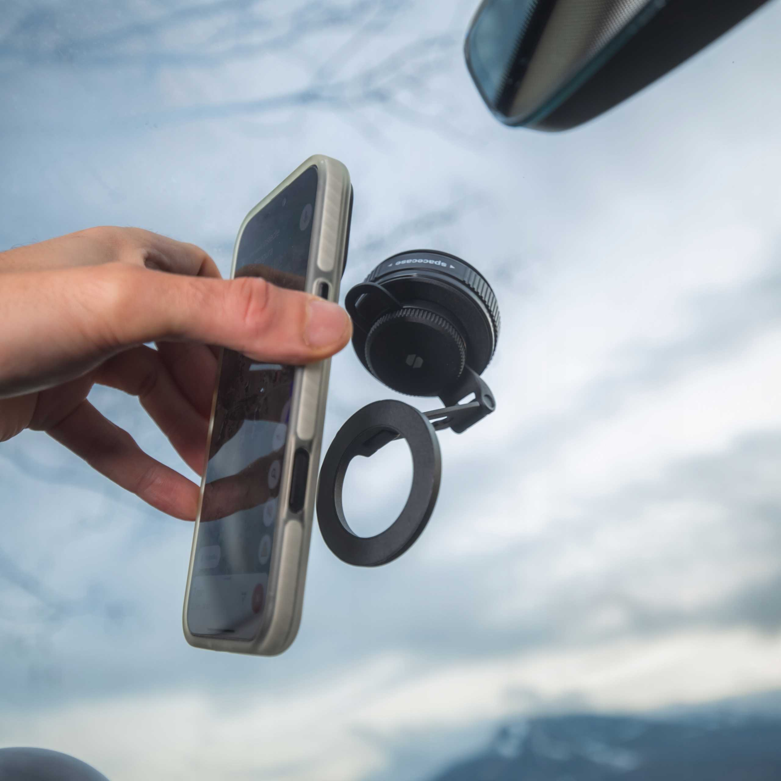 Ręka trzyma telefon z mocowaniem obiektywu, z niebem i górą w tle.