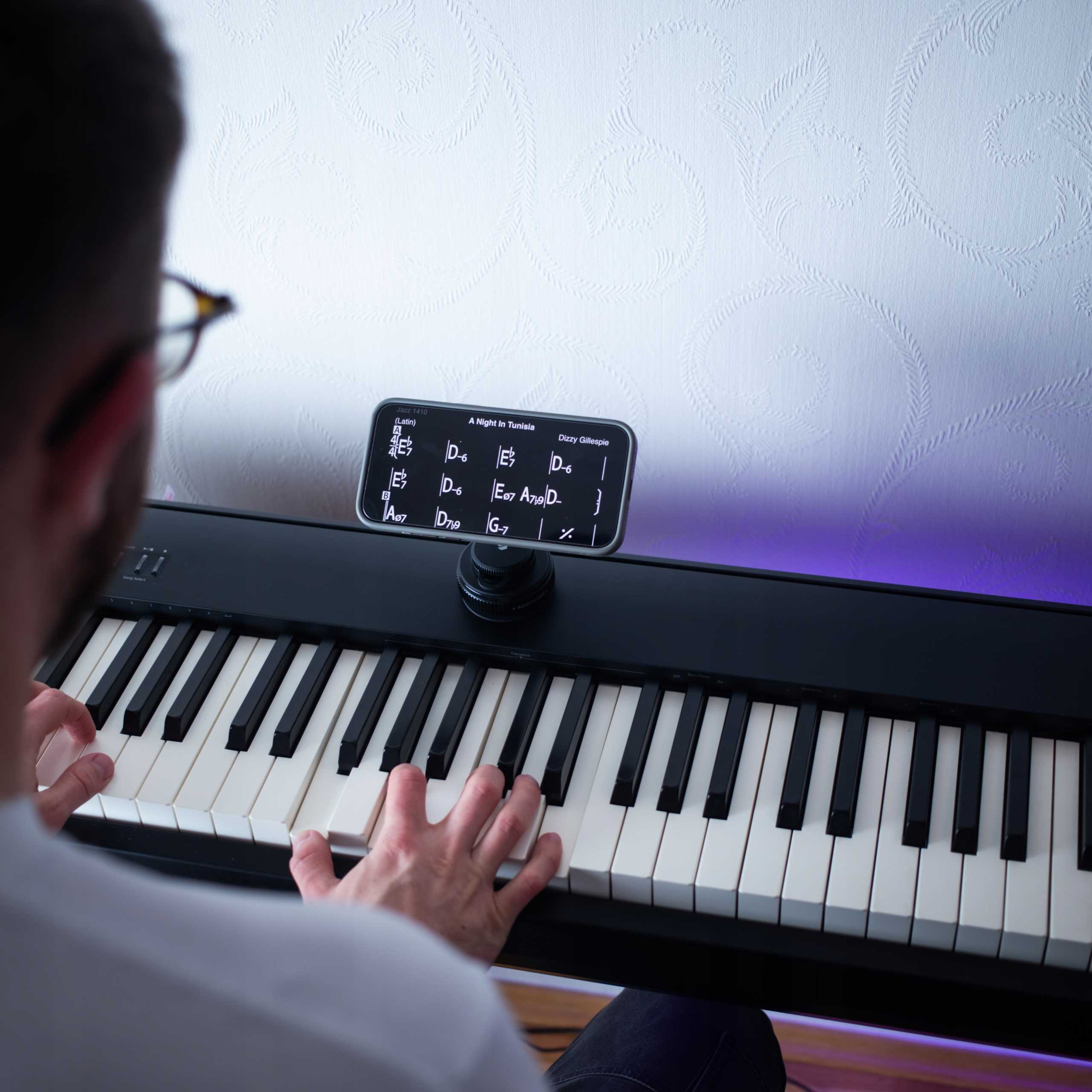 Osoba gra na klawiaturze. Telefon wyświetla nuty. Tło z teksturowanym wzorem.