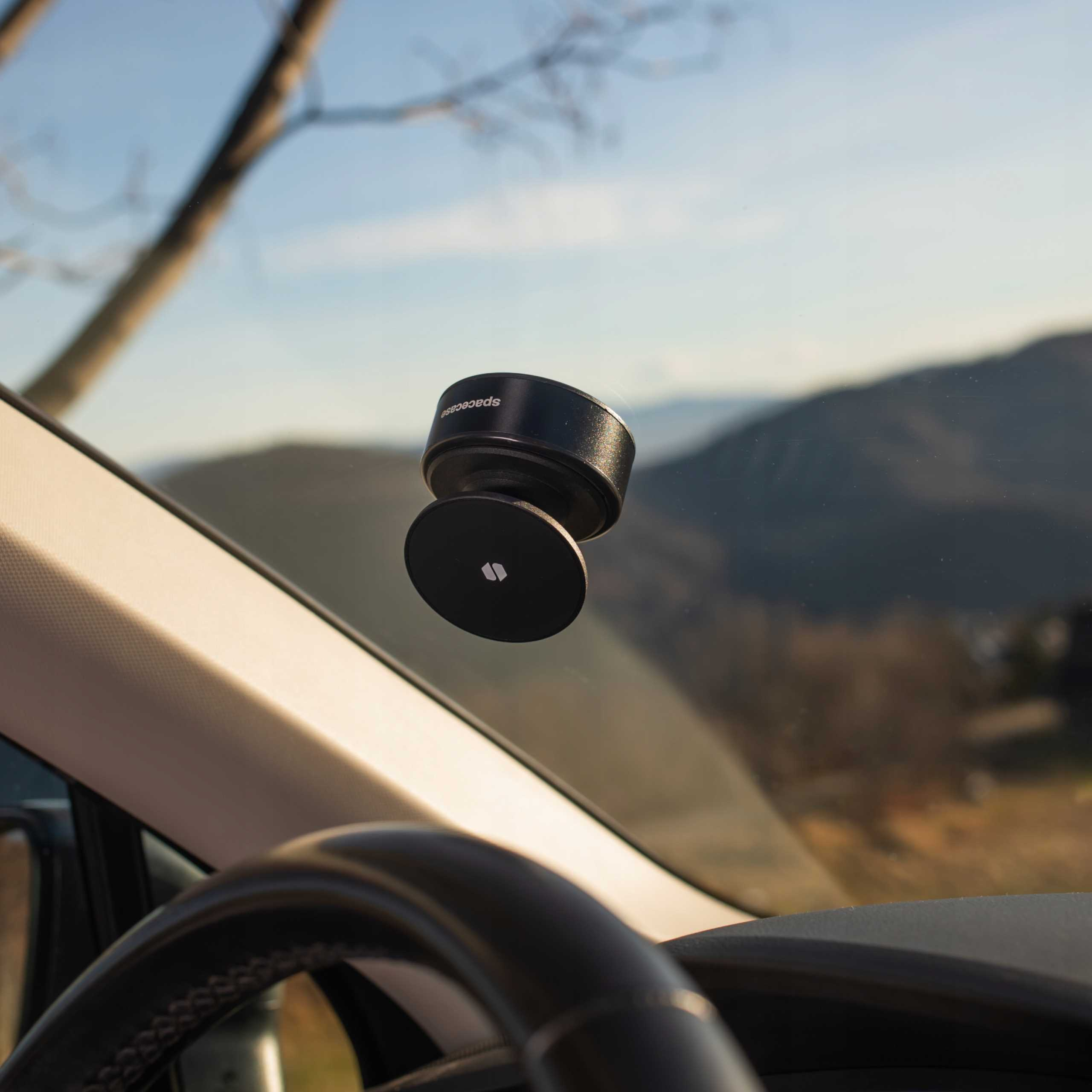 Czarny uchwyt na telefon jest przymocowany do przedniej szyby samochodu. Przez szybę widać góry.