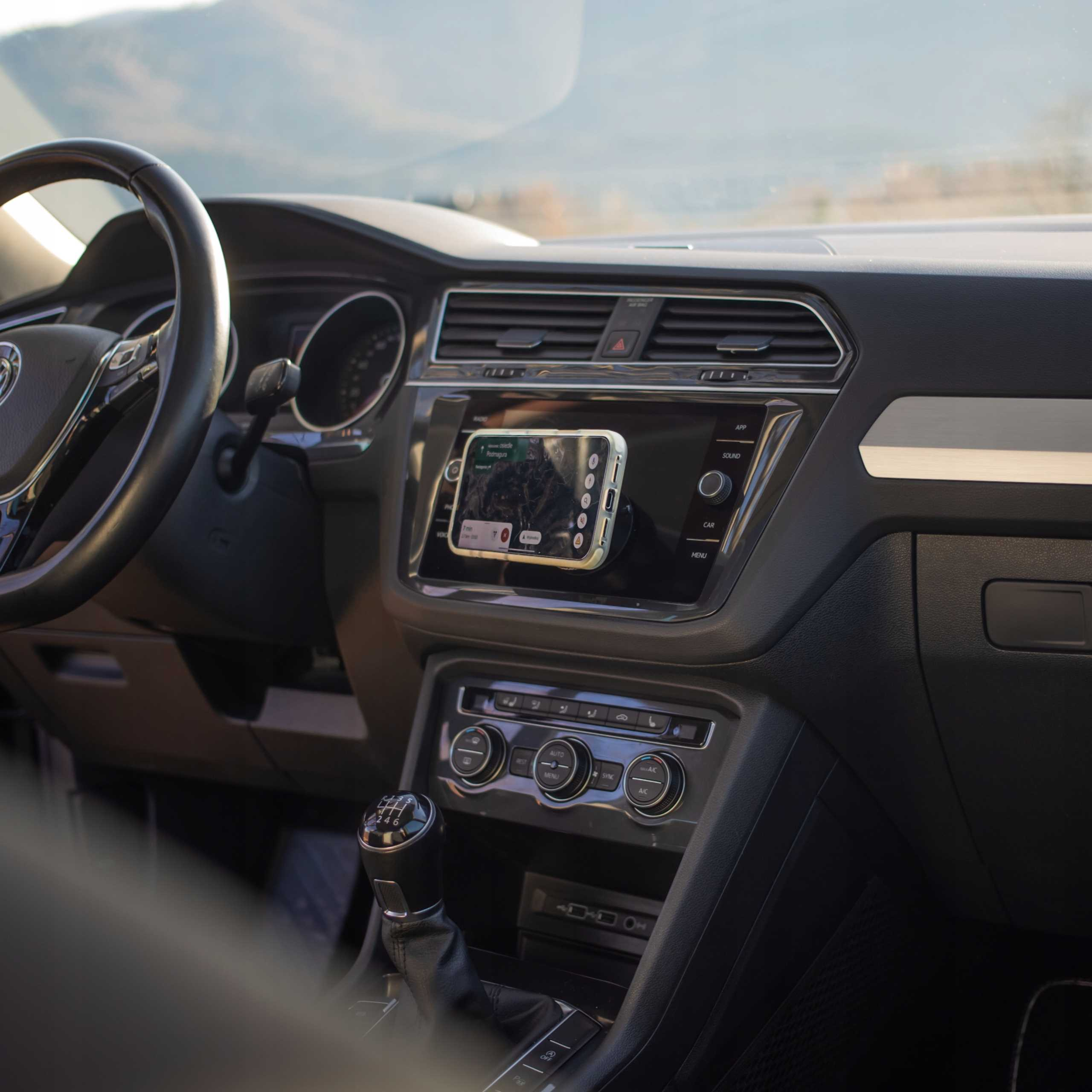 Widok wnętrza samochodu. Telefon z aplikacją nawigacyjną zamontowany na desce rozdzielczej. Widoczna kierownica, dźwignia zmiany biegów i elementy sterujące.