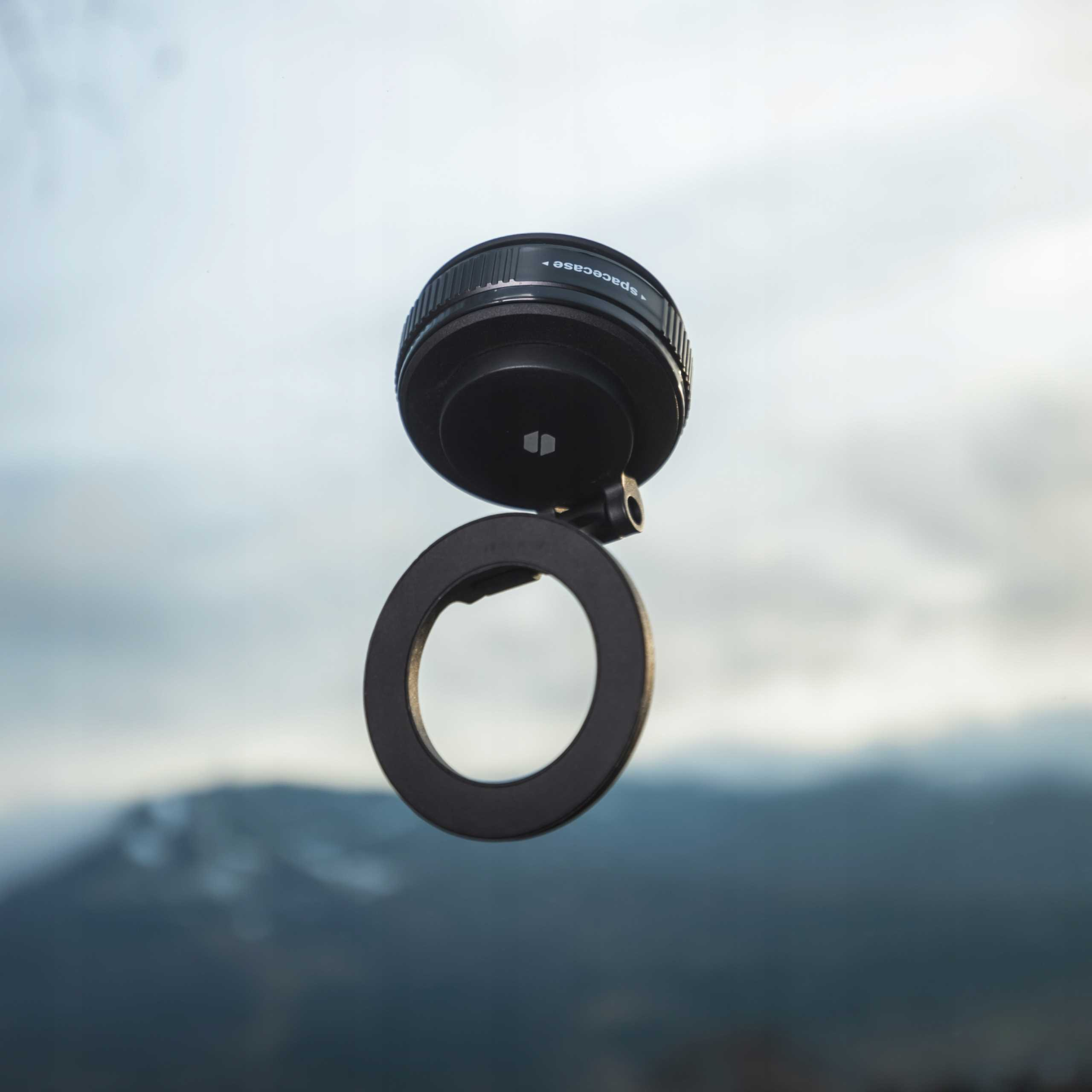 Czarny obiektyw aparatu i okrągły uchwyt zawieszone w powietrzu na tle rozmytego krajobrazu górskiego.