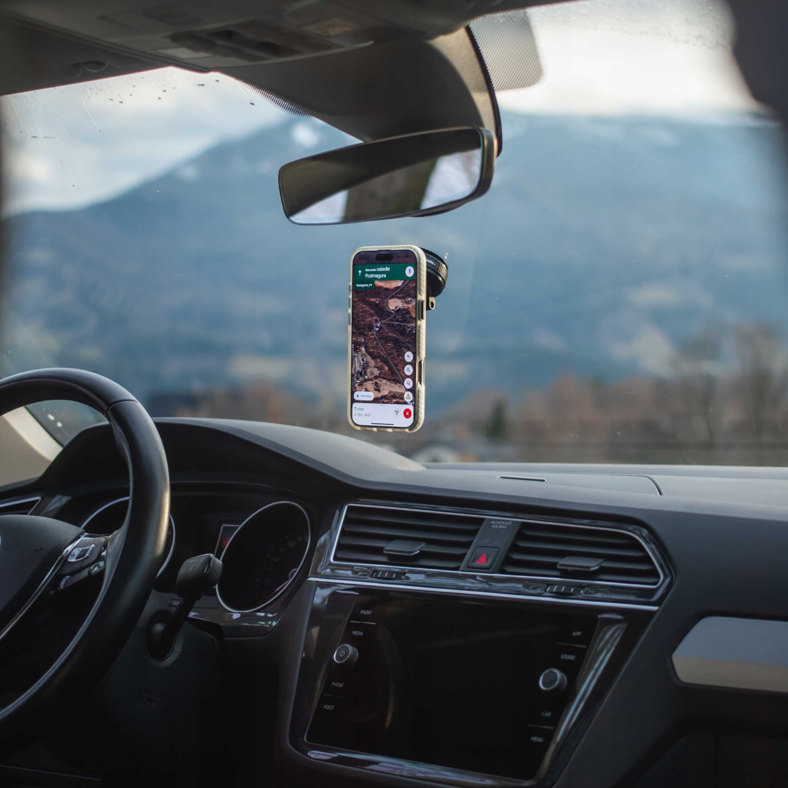 Wewnątrz samochodu telefon wyświetla mapę. Przez przednią szybę widać góry. Widoczna jest również kierownica i deska rozdzielcza.