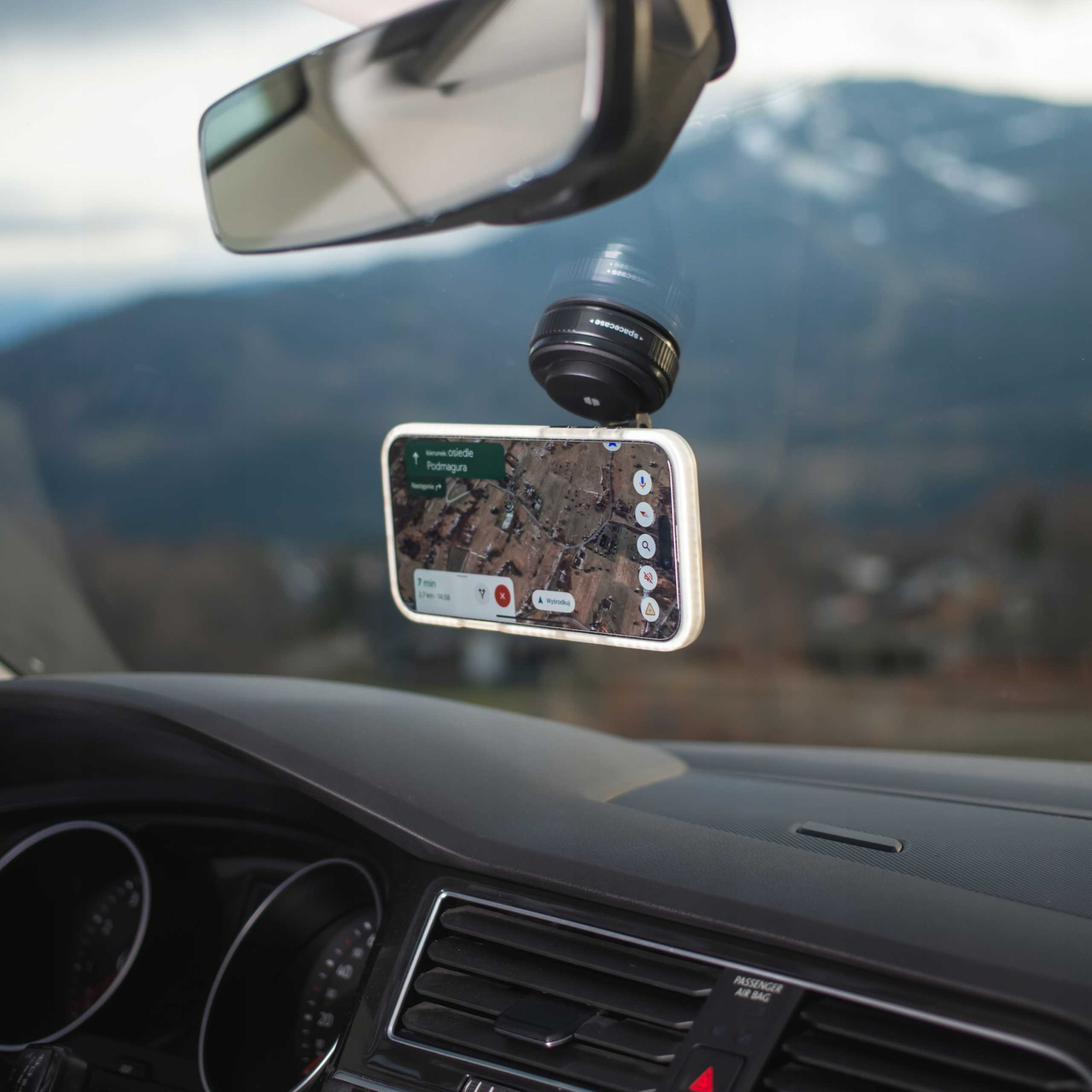 Telefon z mapą jest zamontowany na przedniej szybie samochodu. Obiektyw jest nad nim. Przez przednią szybę widać góry.